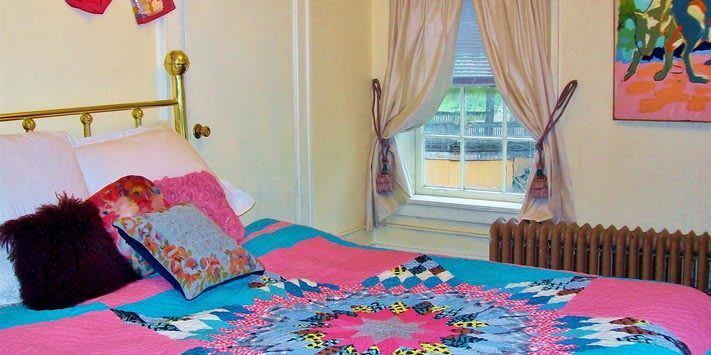 A bed with a pink and blue quilt is in a bedroom next to a window.