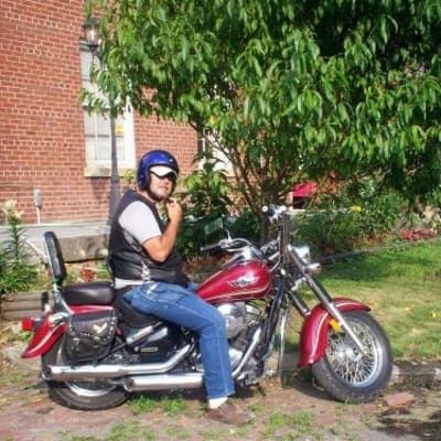 A man is sitting on a red motorcycle in front of a brick building