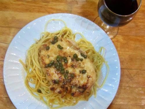 A white plate topped with spaghetti and chicken next to a glass of wine.