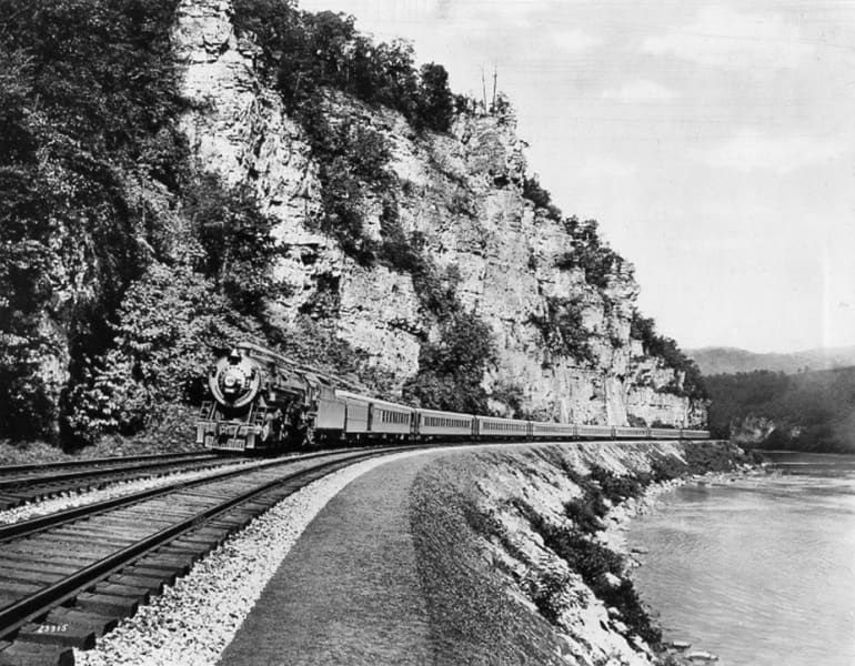 A black and white photo of a train going down the tracks