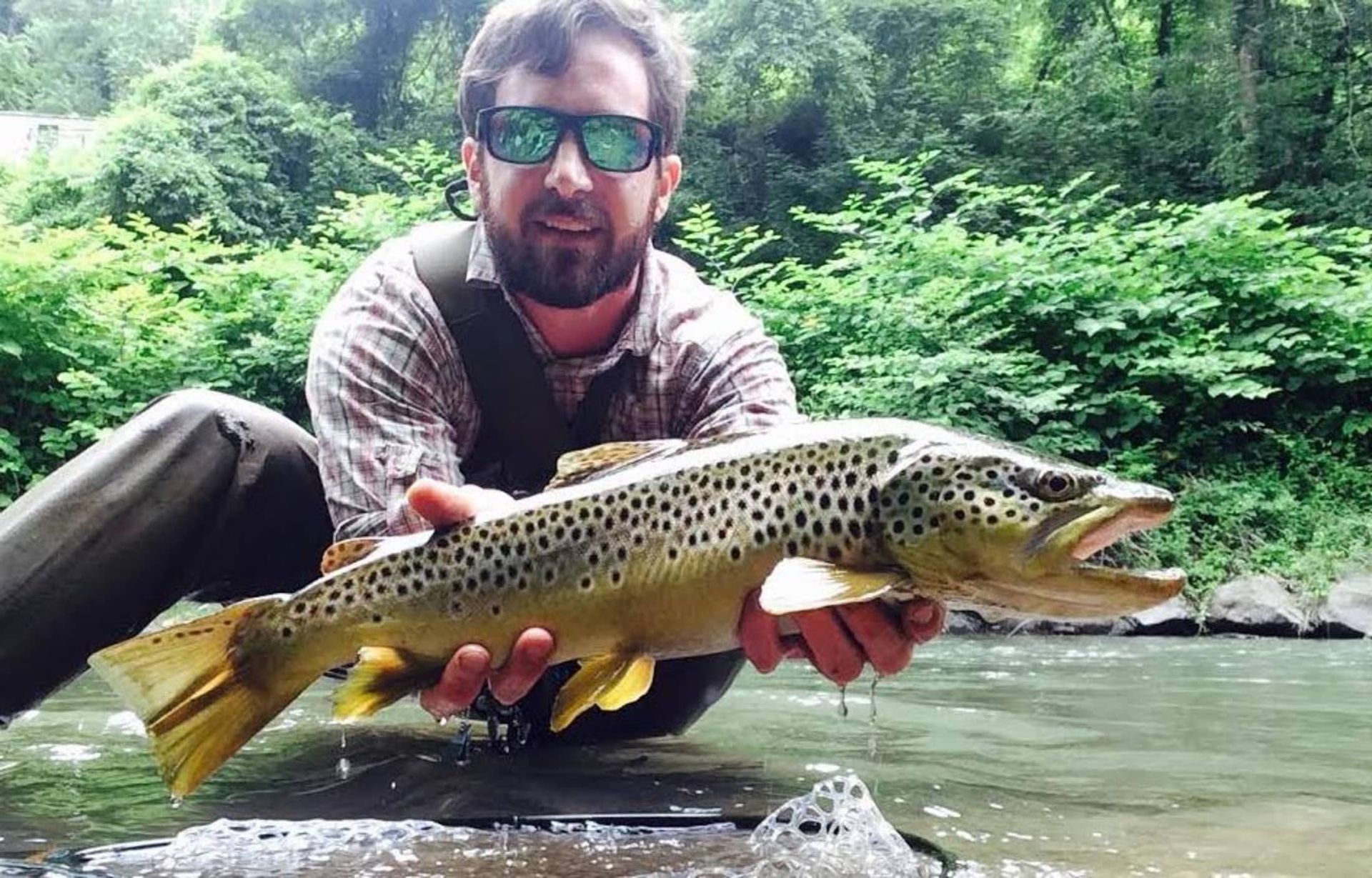 A man is holding a large brown trout in his hands