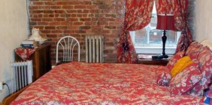 A bedroom with a bed , chair , lamp and a brick wall.