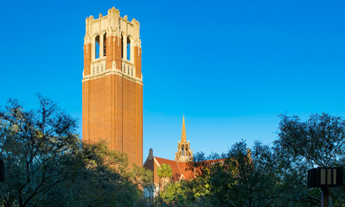 Brick bell tower, part of a university campus, against a blue sky.