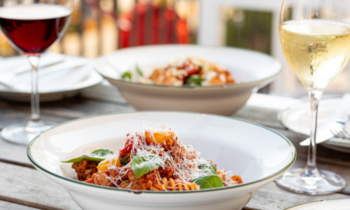 Person spreading caramel-colored spread on a slice of bread outdoors.  A jar of spread and bowl are in the foreground.