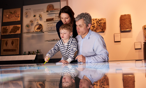 Family in museum, looking at exhibit with child pointing, reflected in the floor.