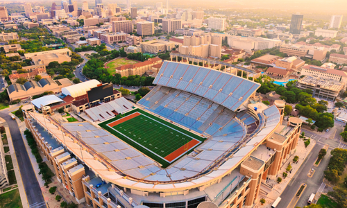 Football player in silver uniform running with the ball on a green field at night.