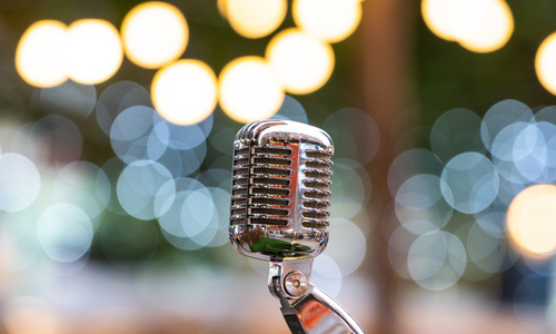 Close-up of a drummer playing a drum kit on stage. Sticks strike drums and cymbals, a blurred band in the background.