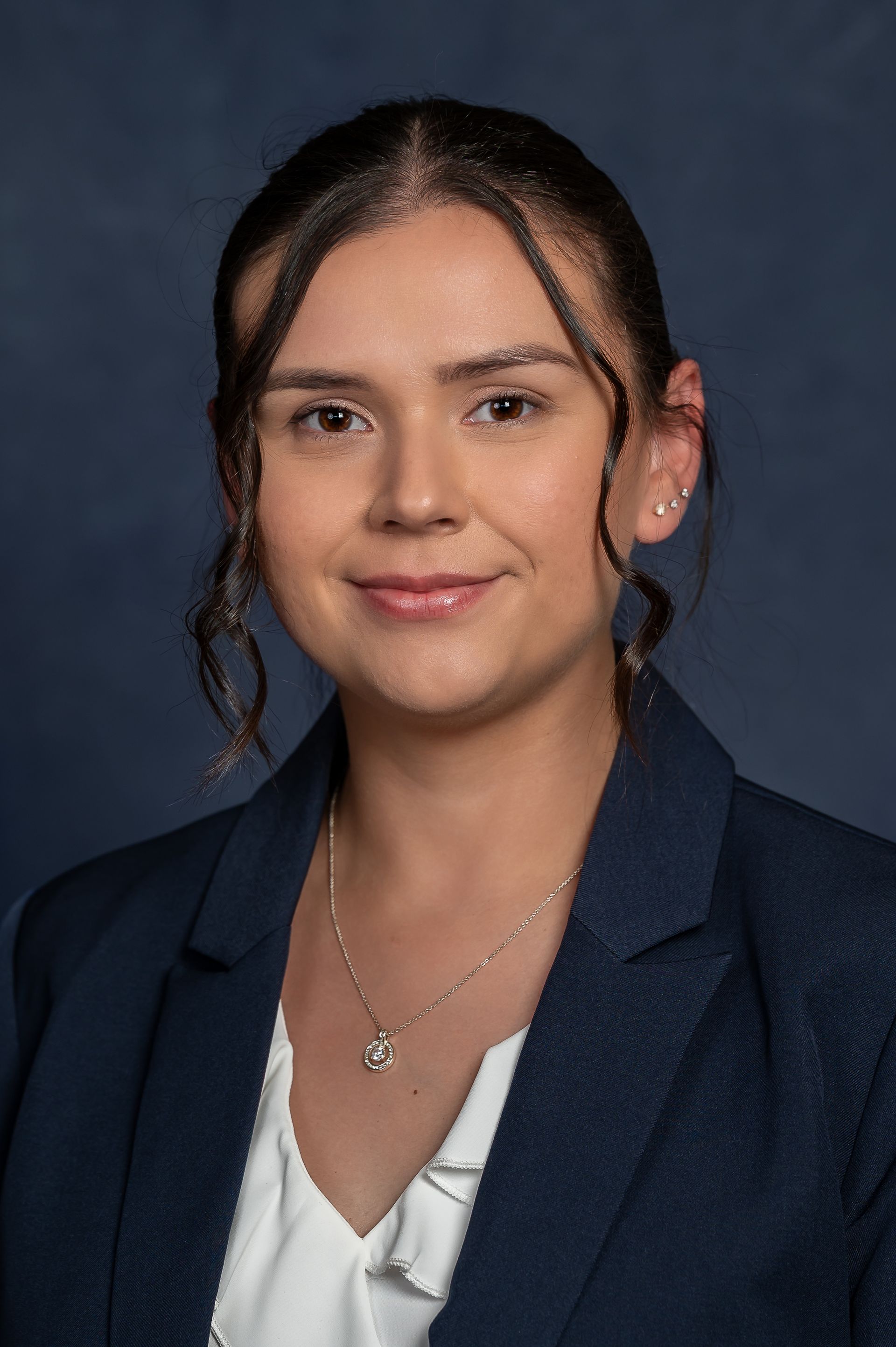 Woman with dark hair in a navy blazer smiles at the camera, wearing a necklace.