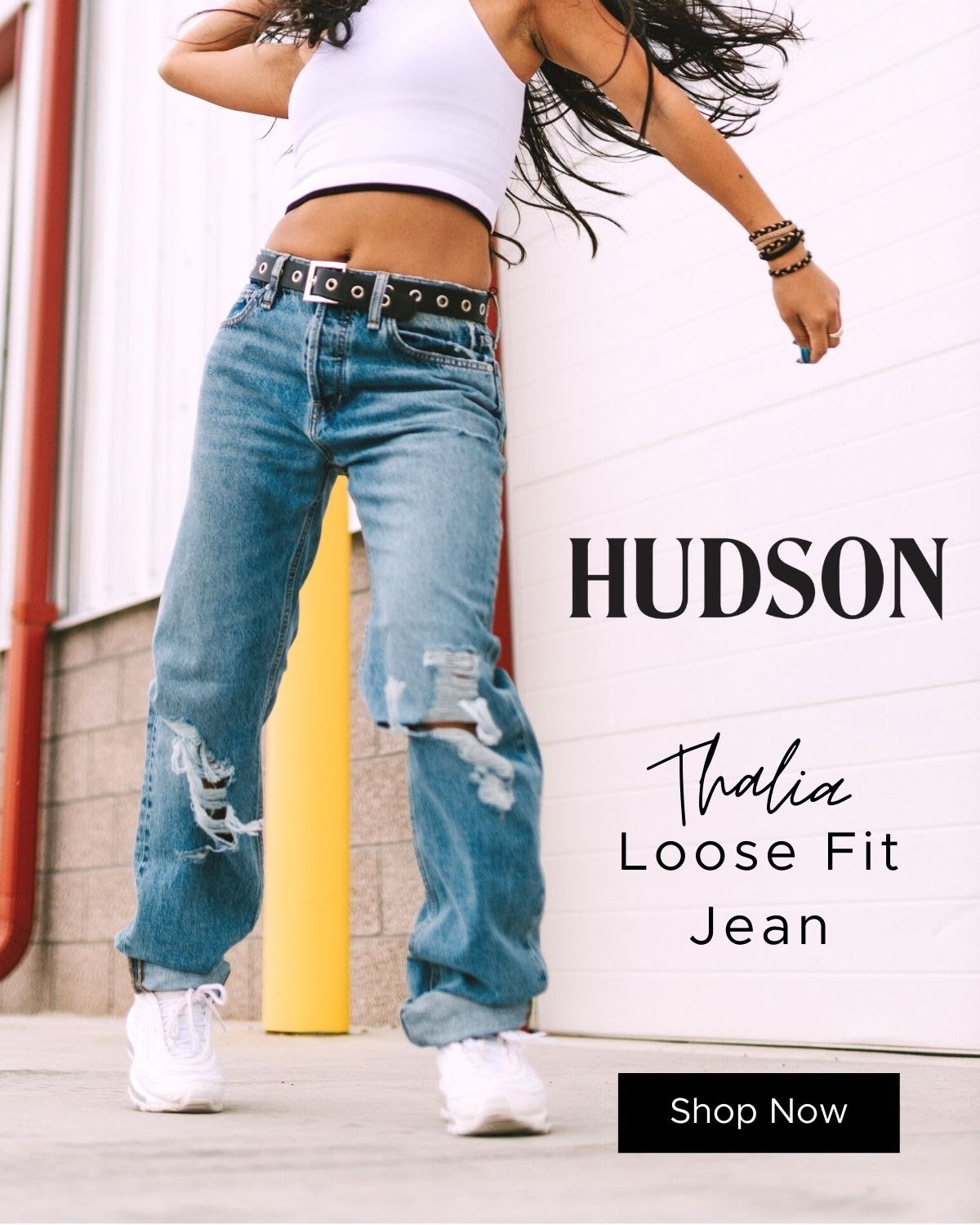 A woman is wearing loose fit jeans and a white tank top.