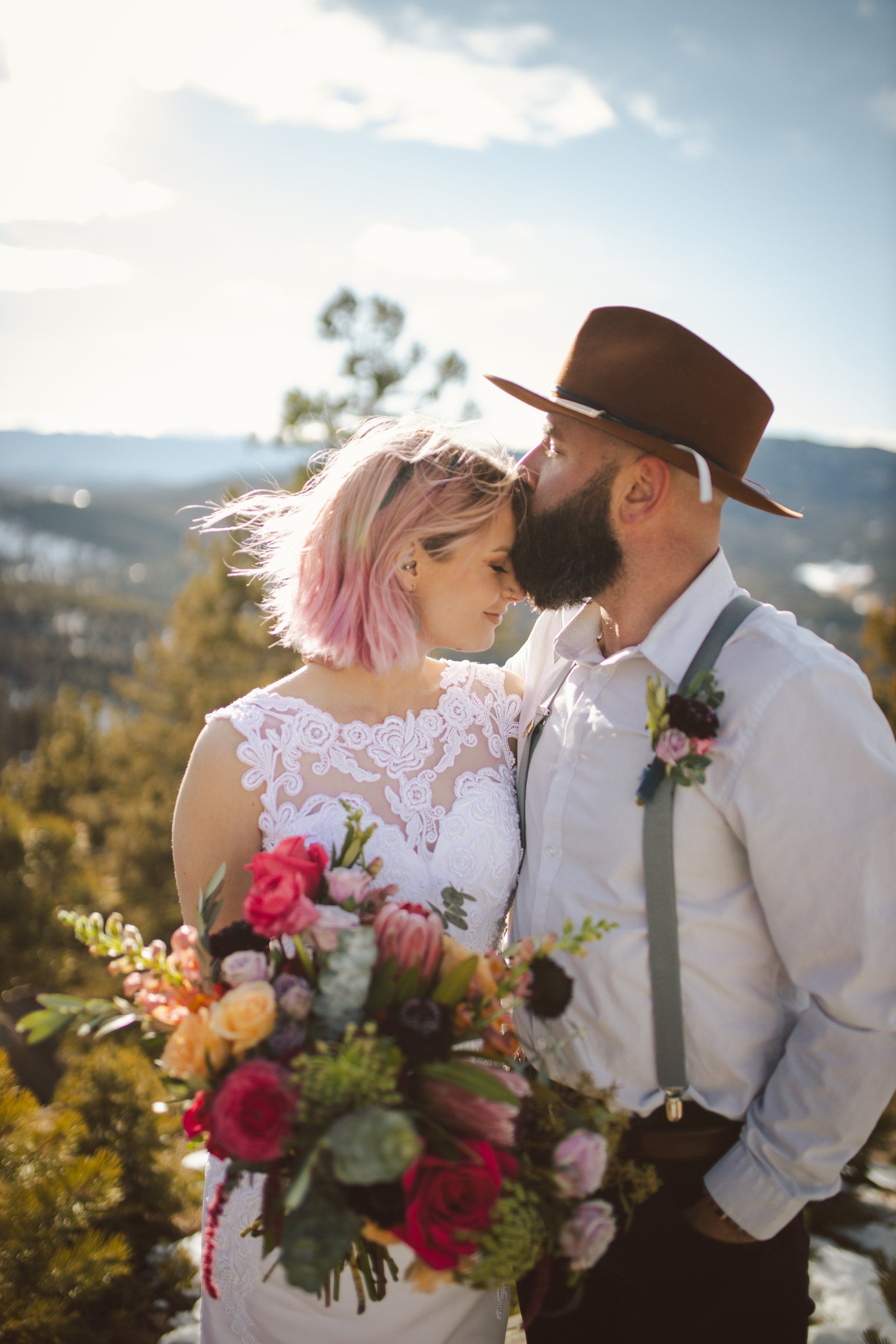 A bride and groom are kissing on top of a mountain.