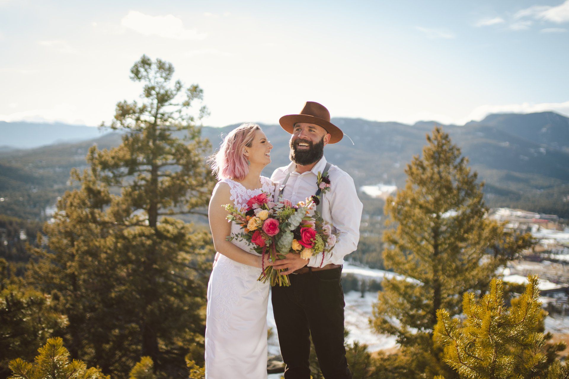 A bride and groom are posing for a picture on top of a mountain.