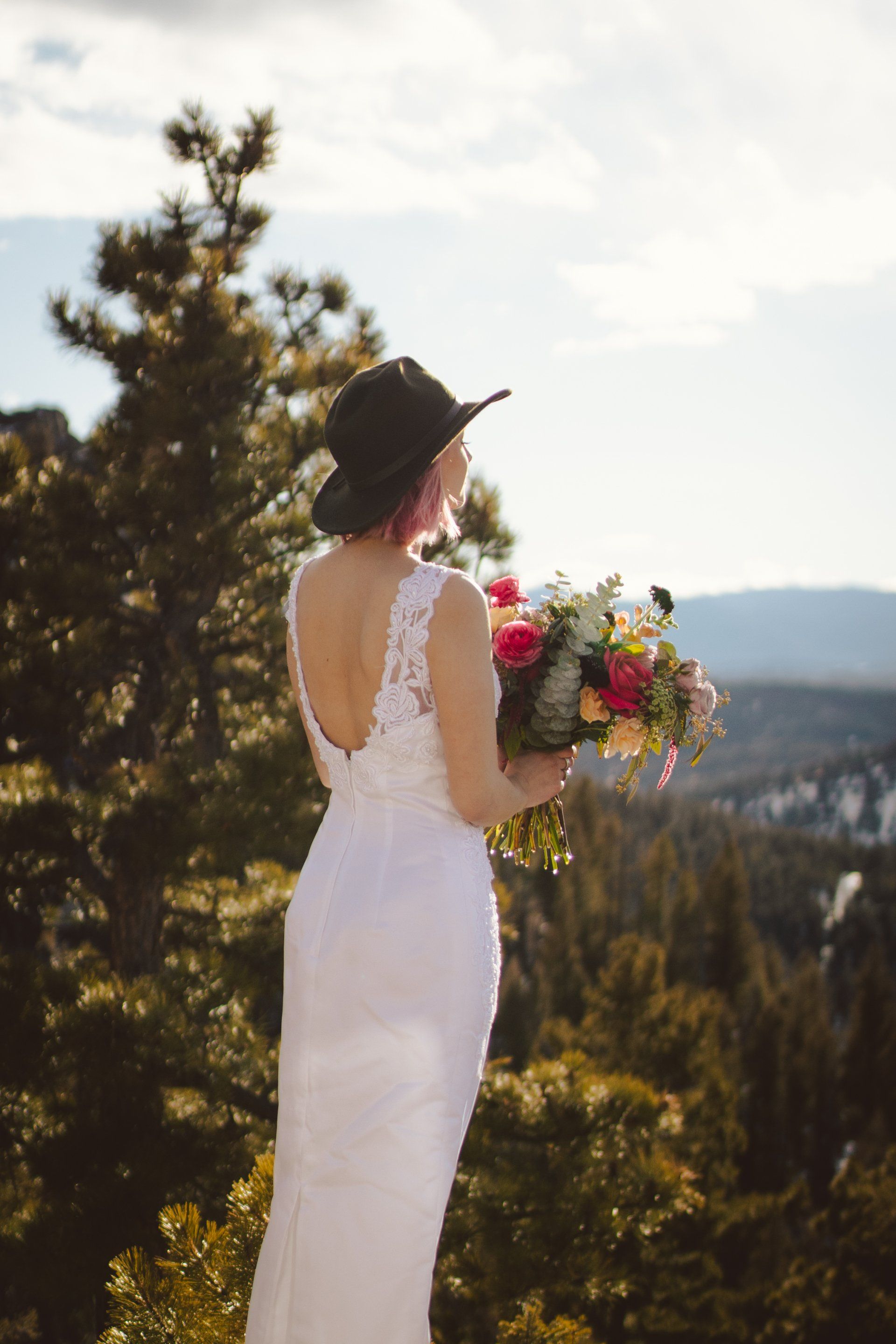A bride in a white dress and black hat is holding a bouquet of flowers.