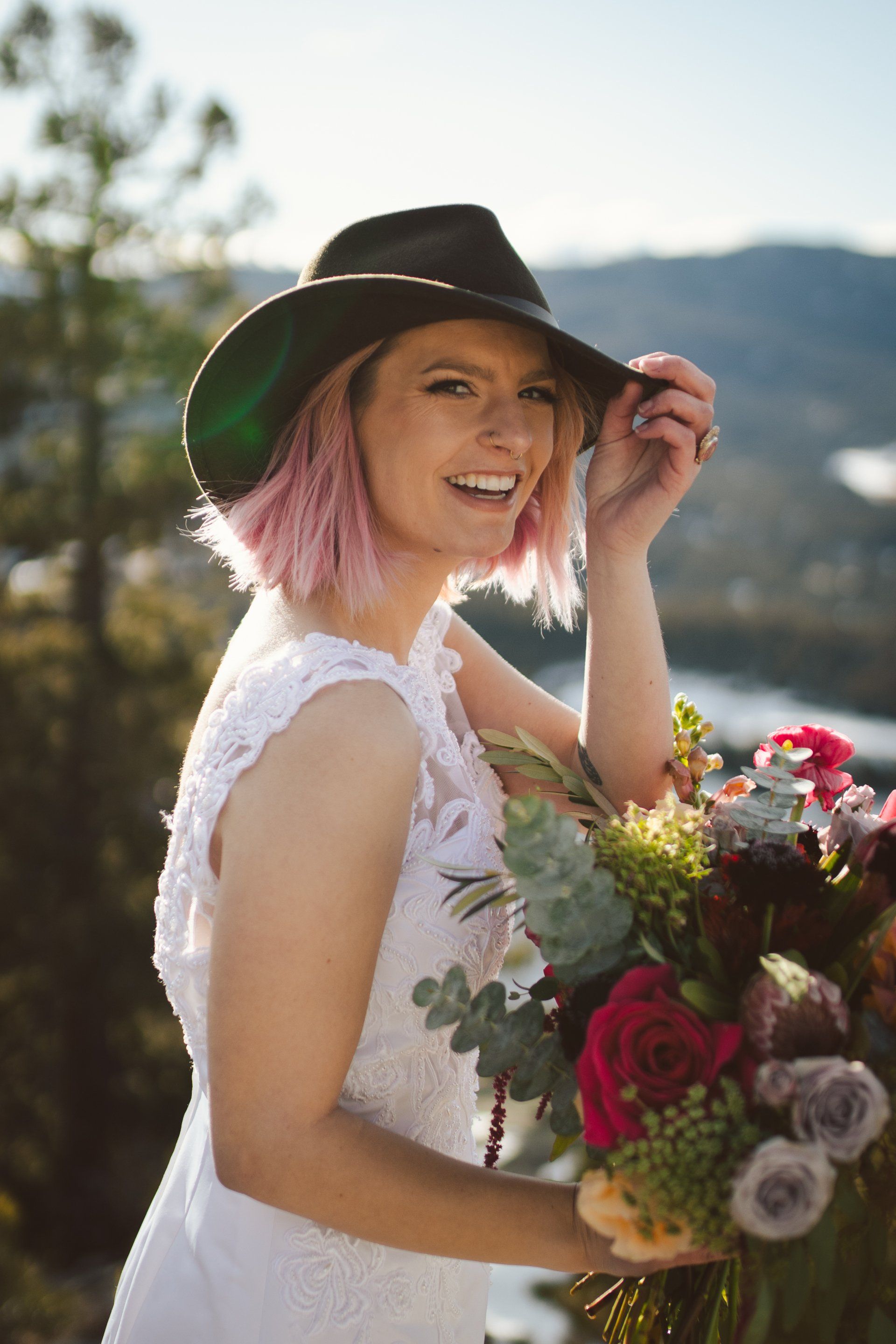 A woman in a white dress and cowboy hat is holding a bouquet of flowers.