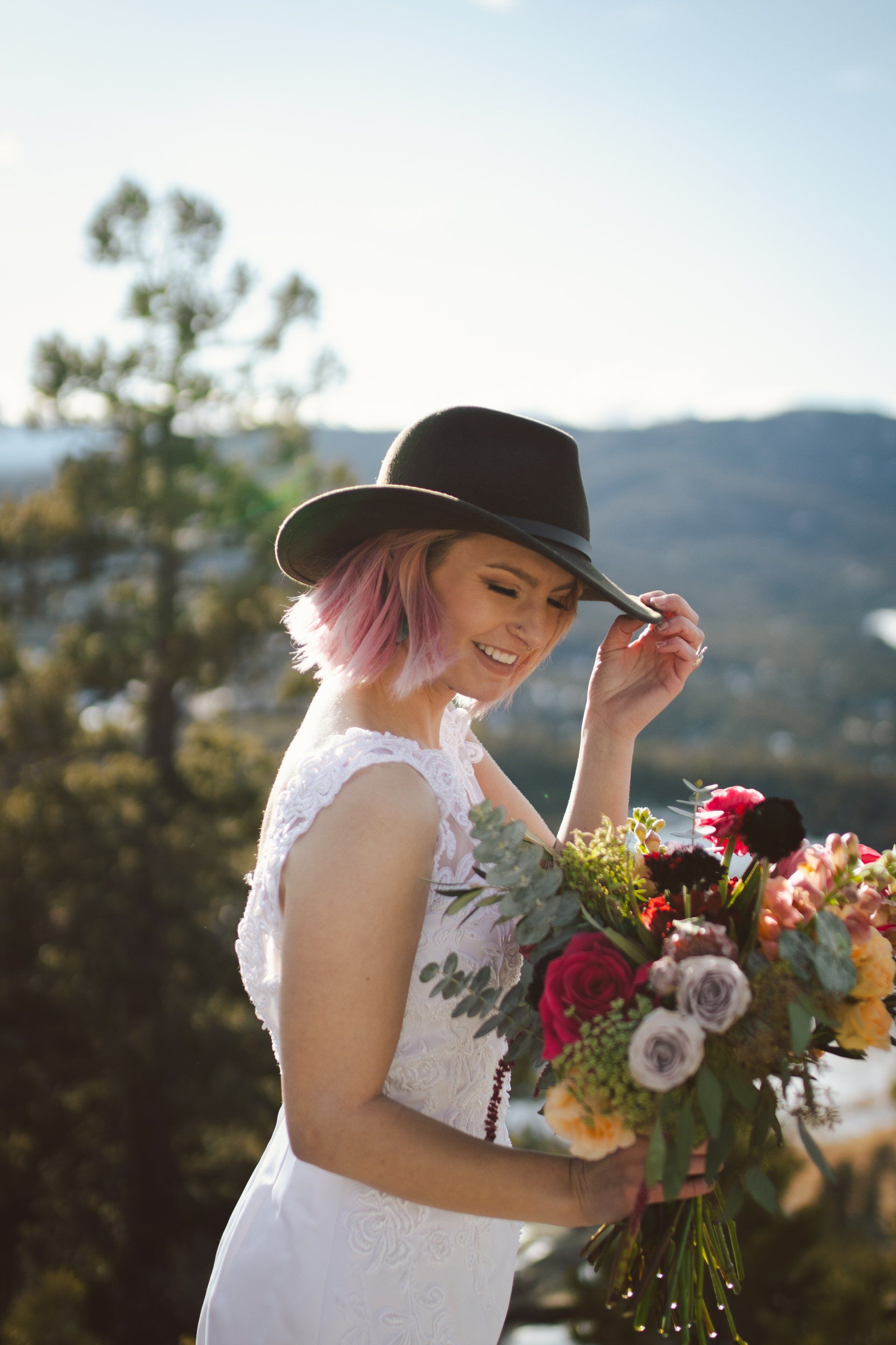 A woman in a white dress and black hat is holding a bouquet of flowers.