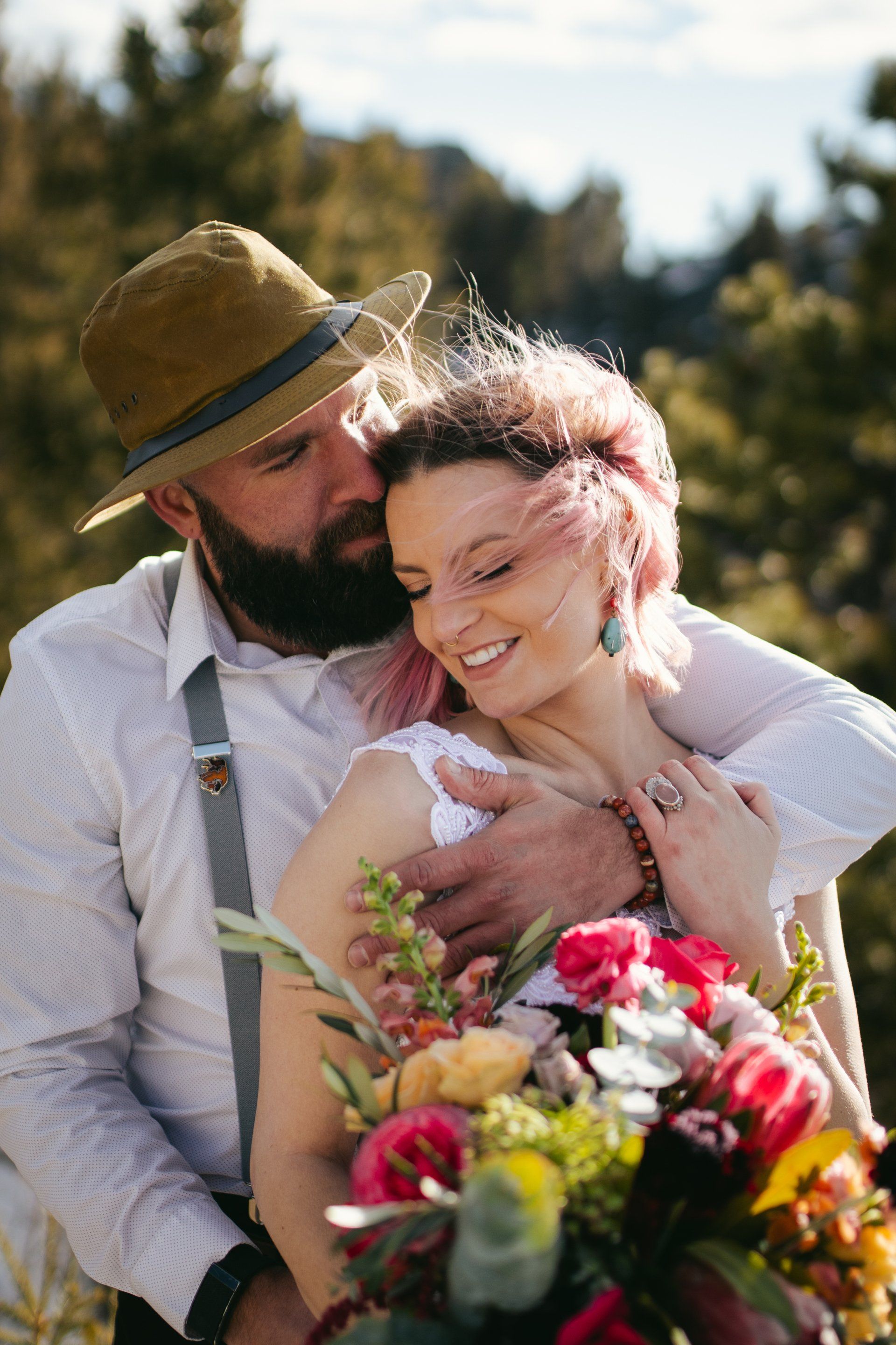A bearded man is hugging a woman with pink hair and a bouquet of flowers.