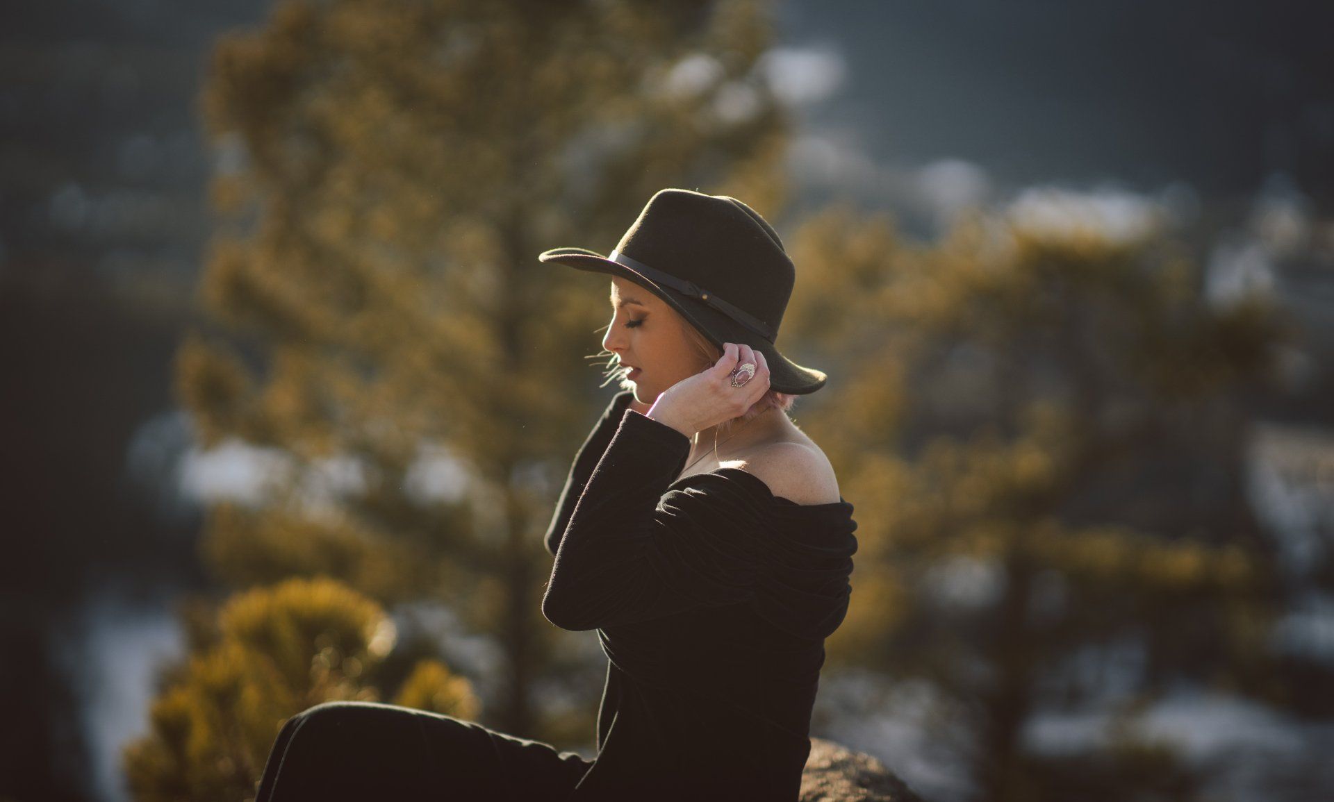 A woman in a black dress and hat is sitting on a rock.