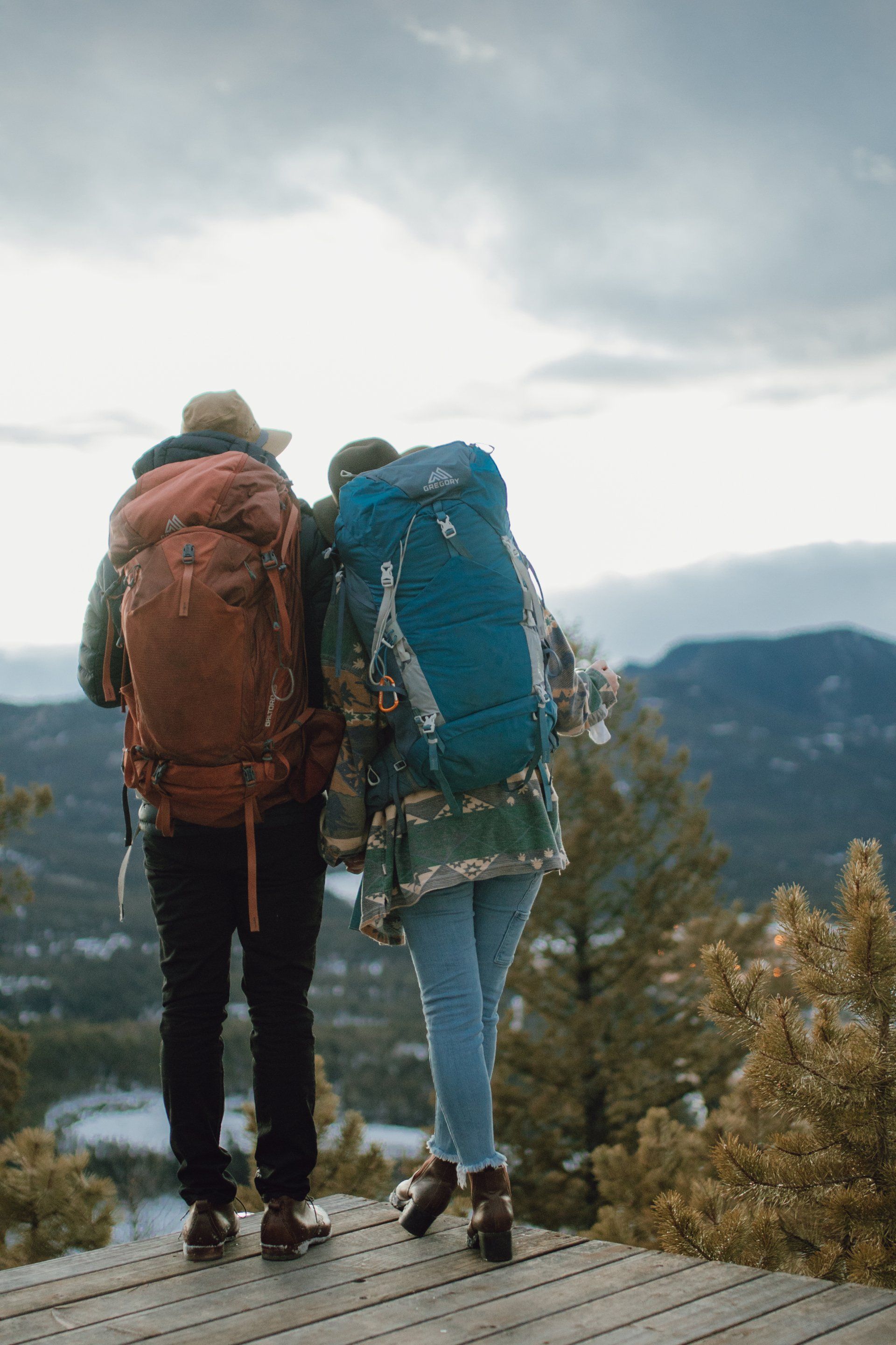 A man and a woman with backpacks are standing on top of a wooden deck.
