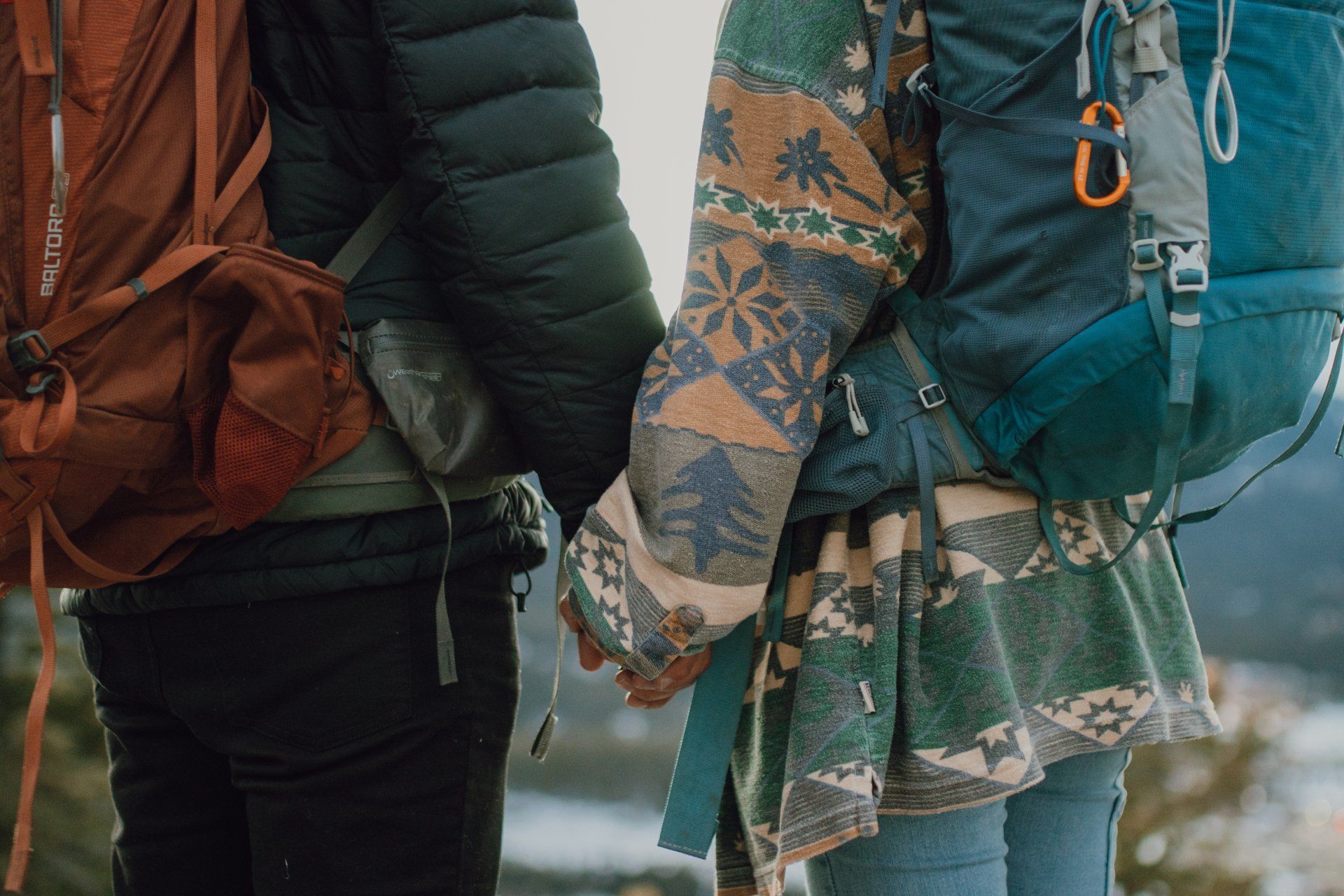 A man and a woman with backpacks are holding hands.