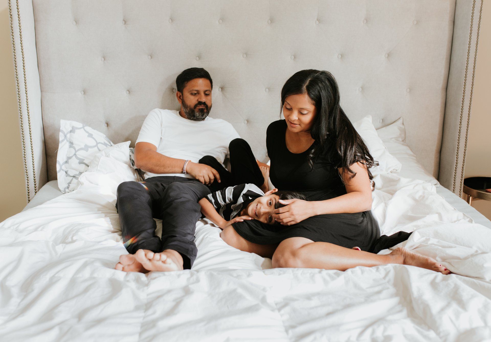 A man , woman and child are sitting on a bed.