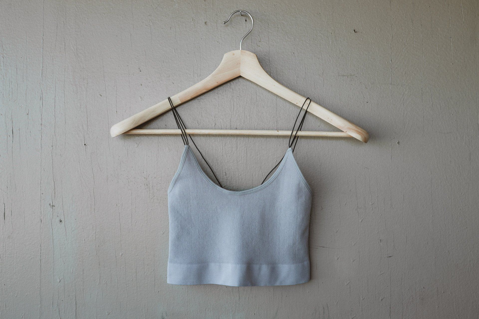 A gray crop top is hanging on a wooden hanger.