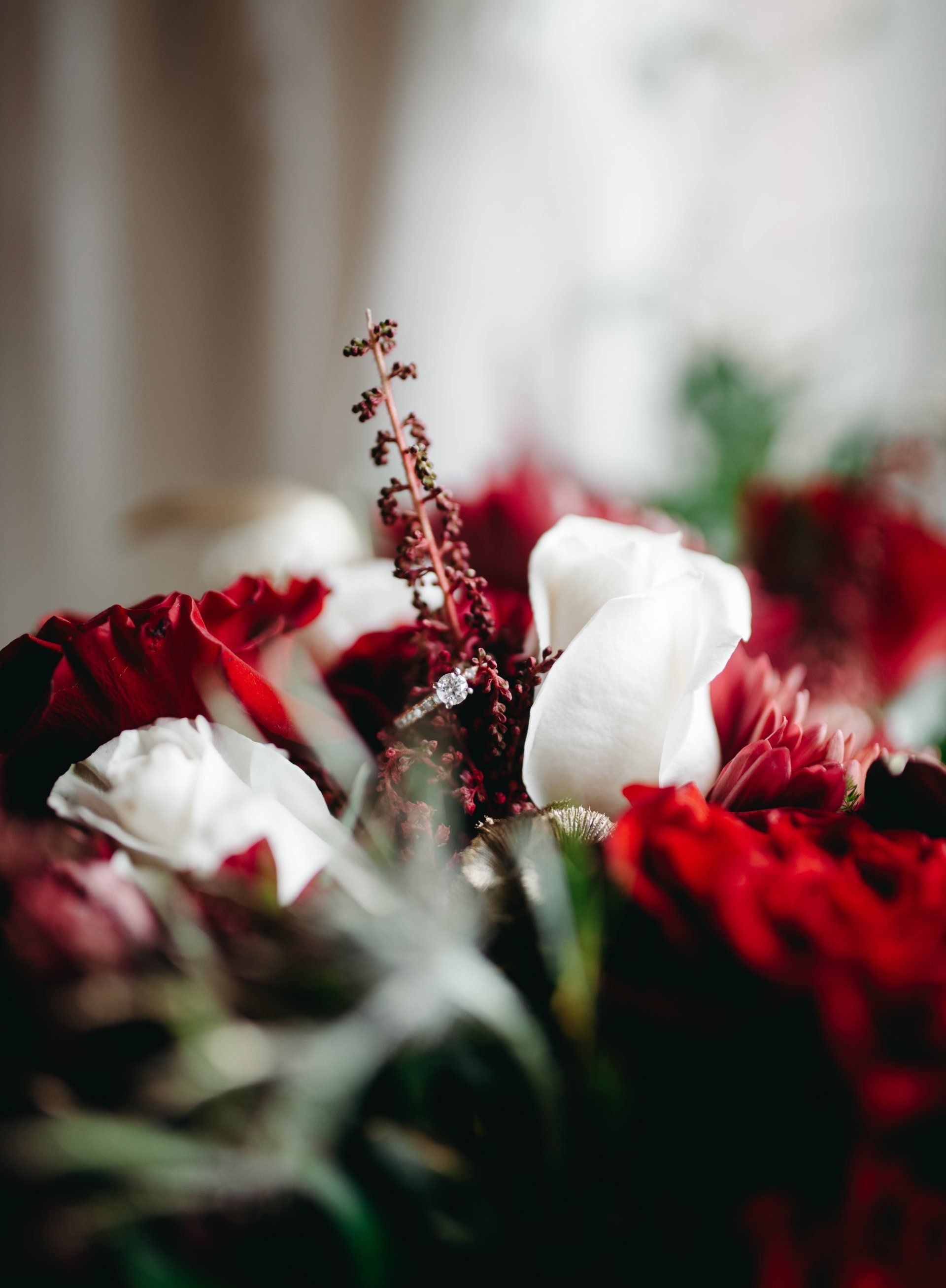 A close up of a wedding ring in a bouquet of red and white flowers.