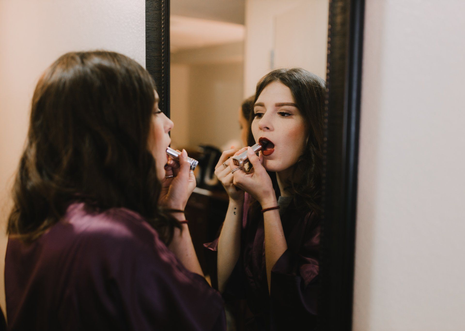 A woman is applying lipstick in front of a mirror.