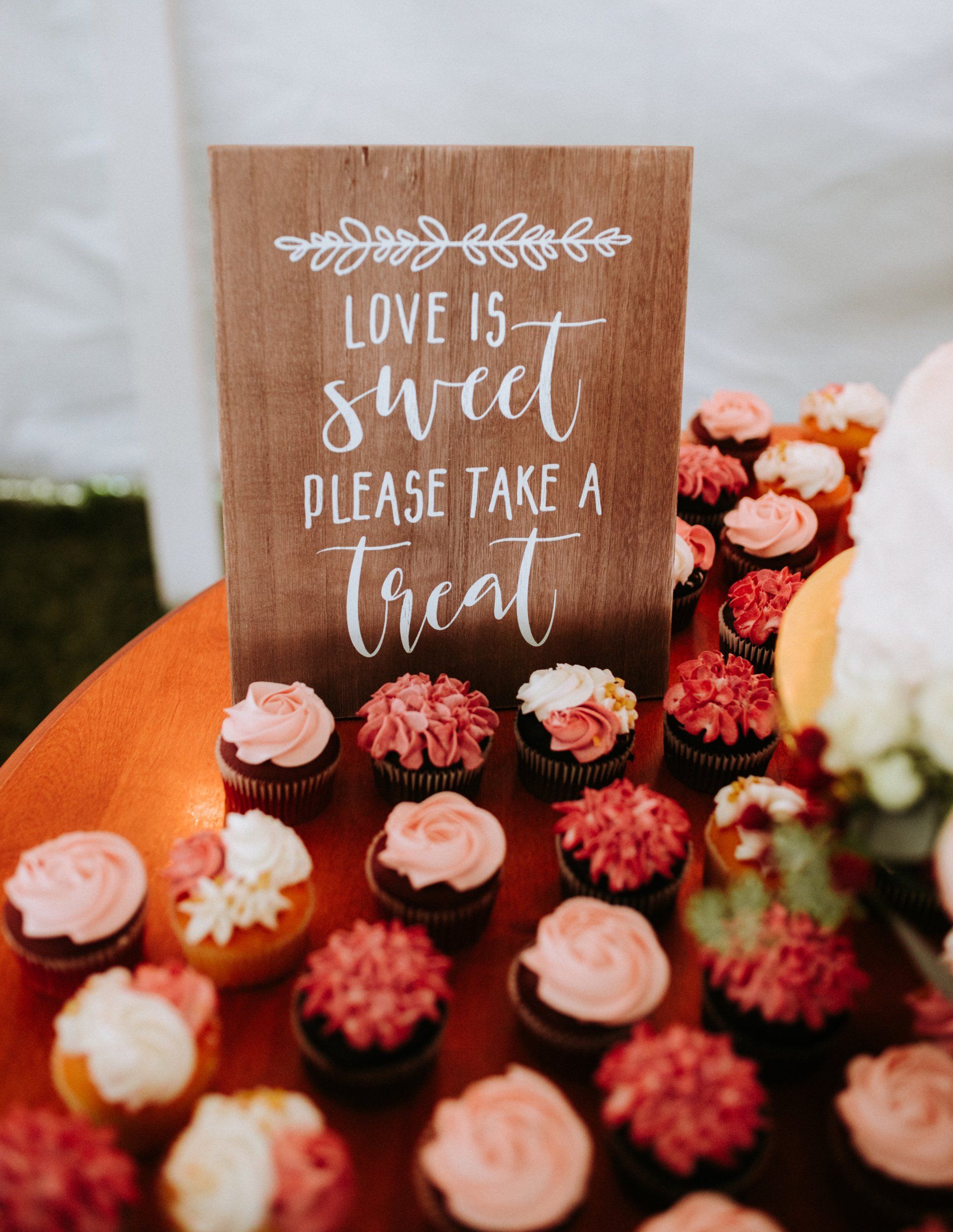 A table topped with cupcakes and a sign that says `` love is sweet please take a treat ''