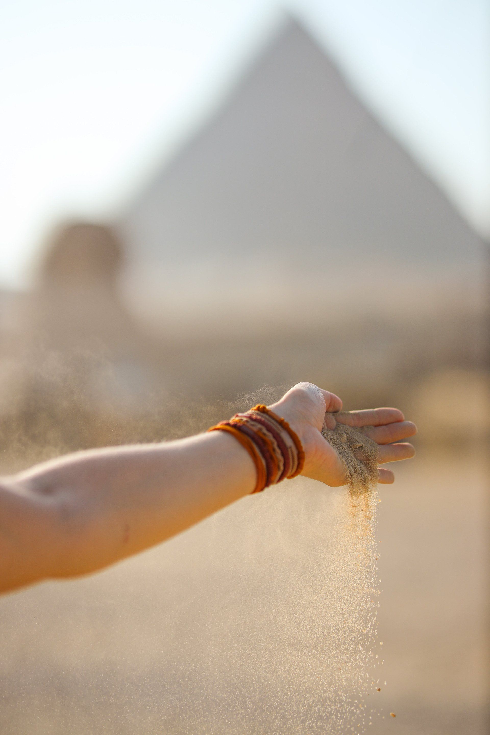 A woman is pouring sand from her hand in front of a pyramid.