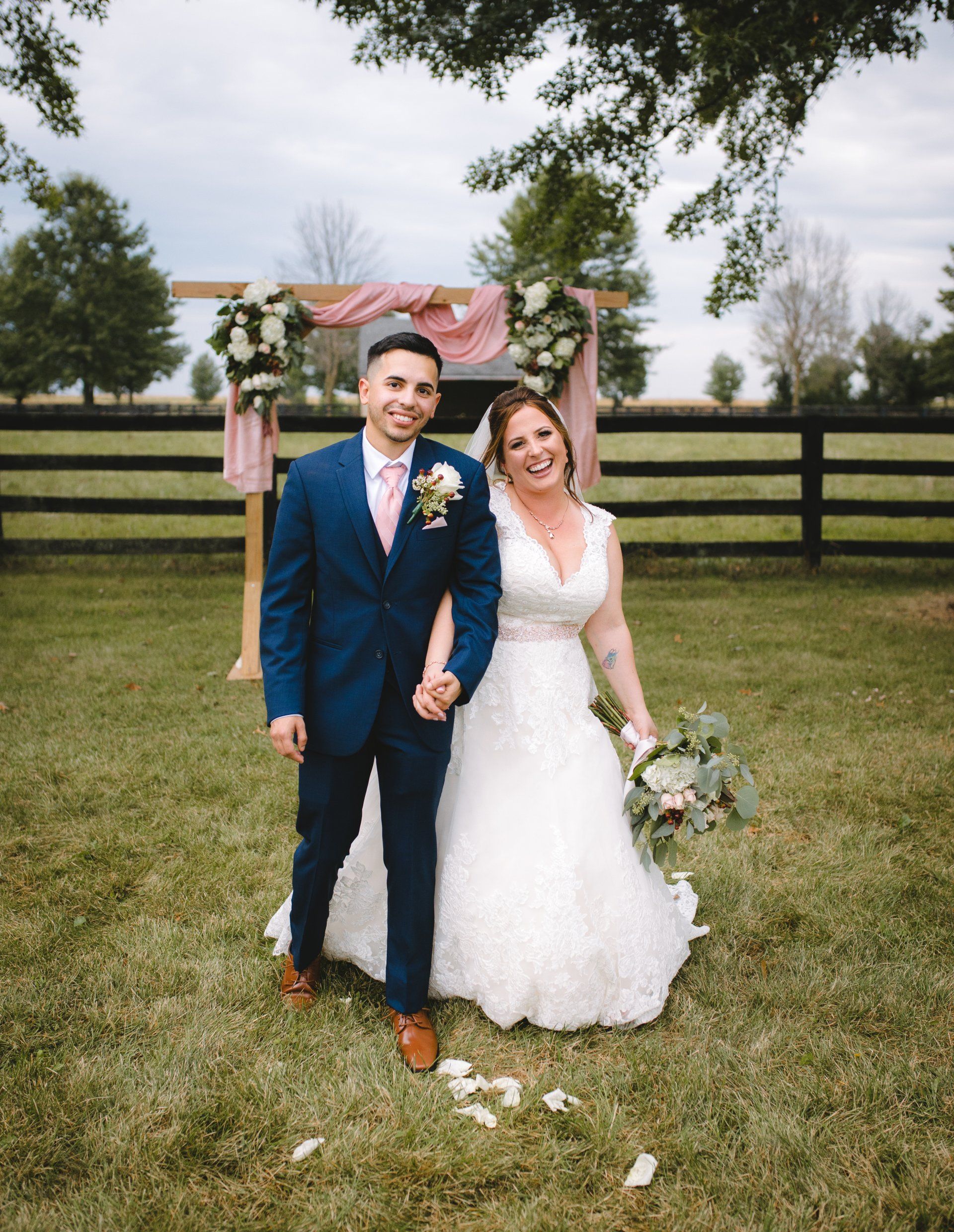 A bride and groom are standing in the grass holding hands.