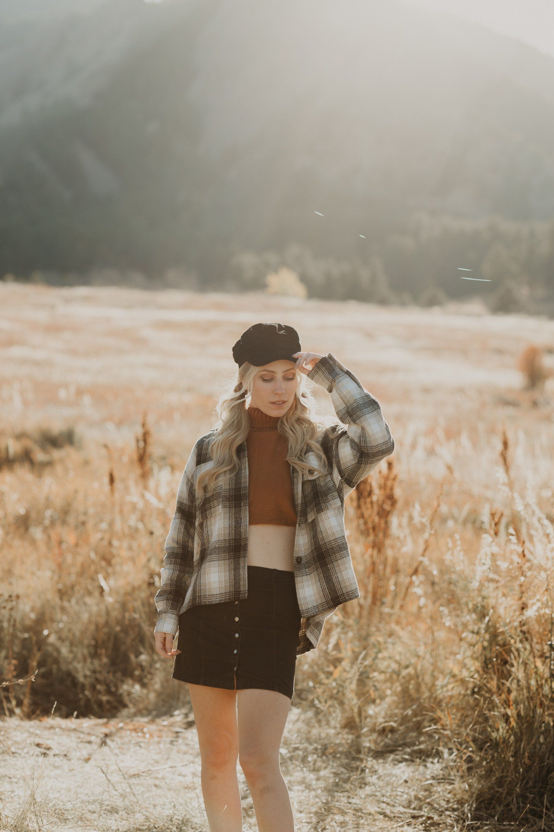 A woman in a plaid shirt and black skirt is standing in a field.