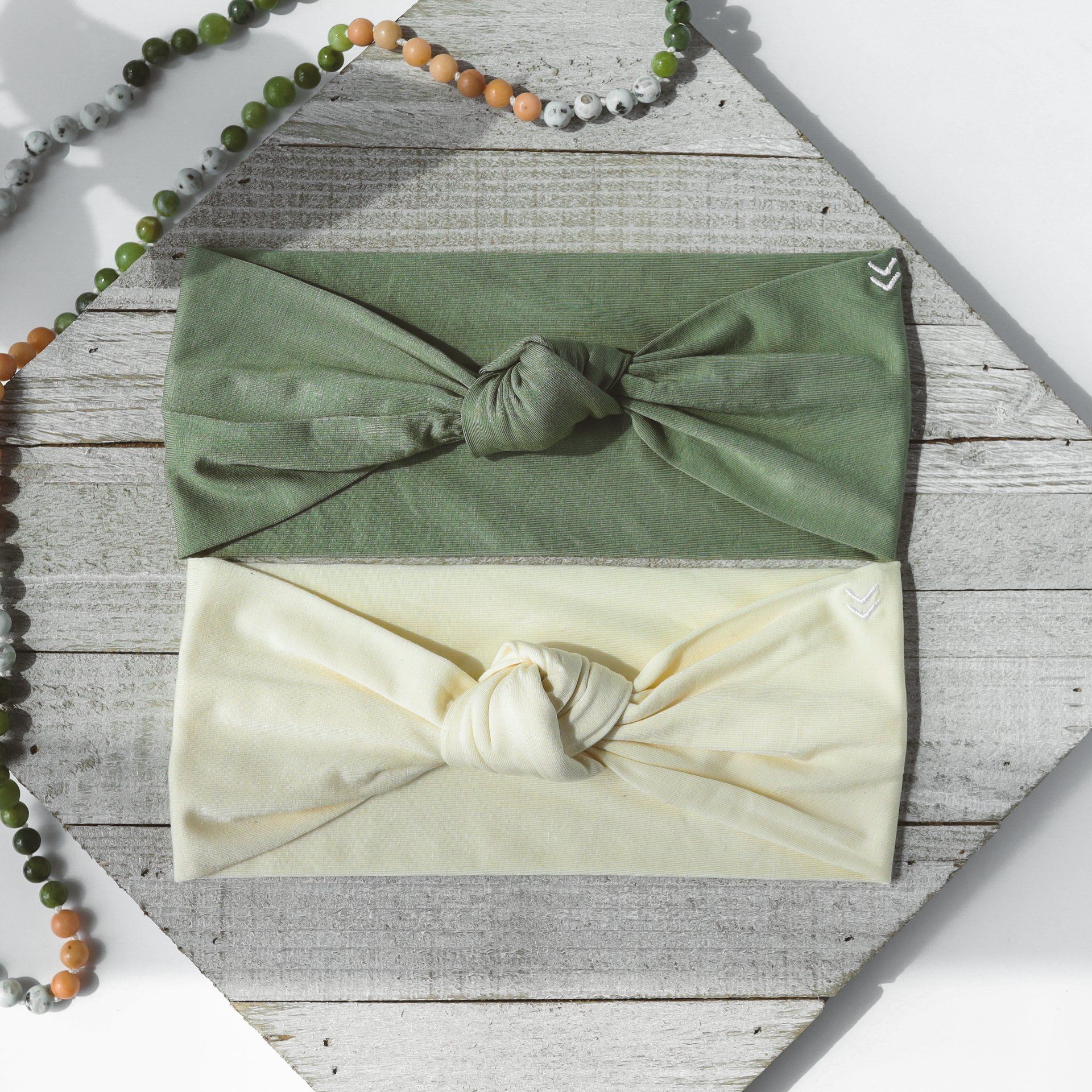 Two headbands are sitting on a wooden table next to a necklace.