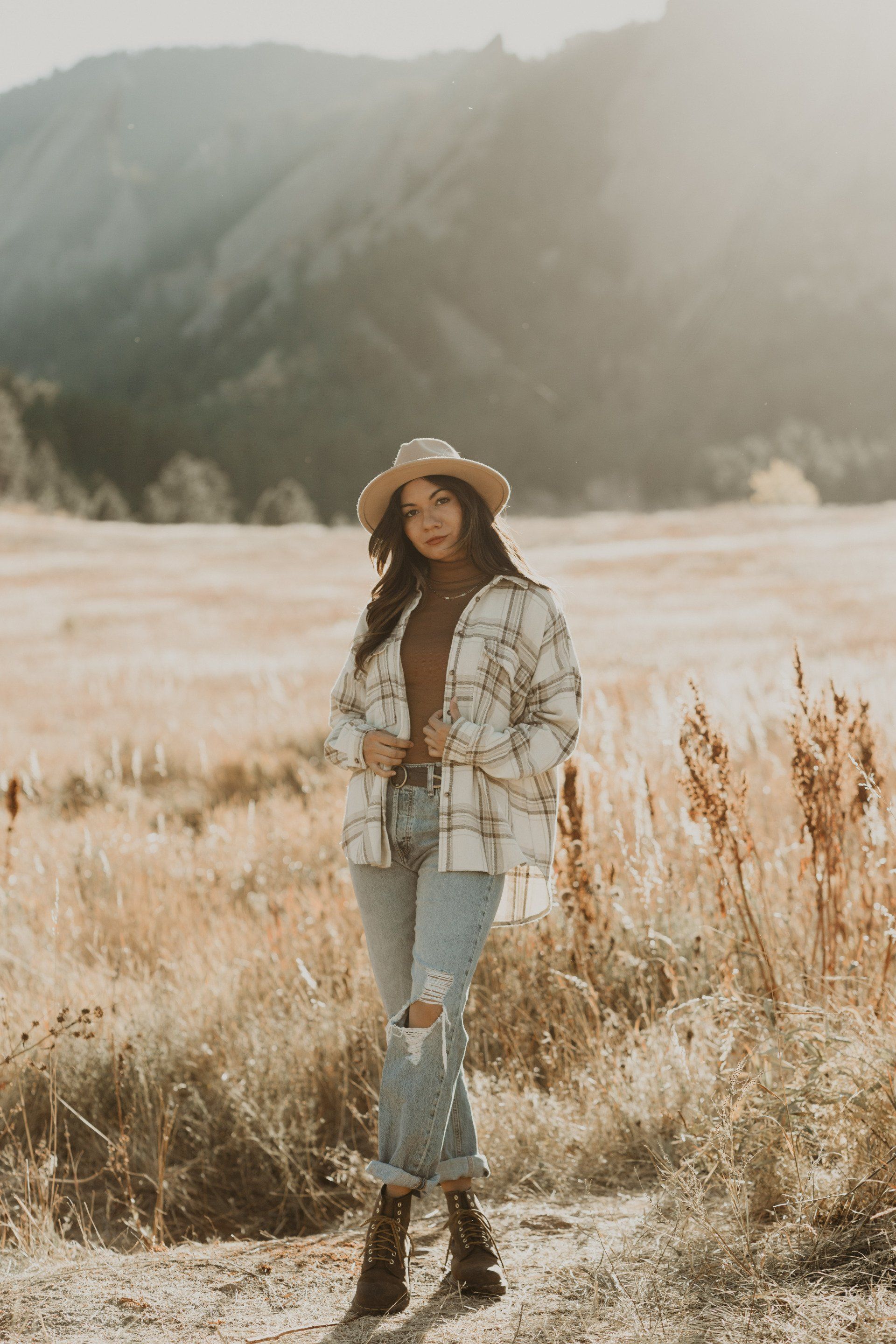 A woman is standing in a field with mountains in the background.