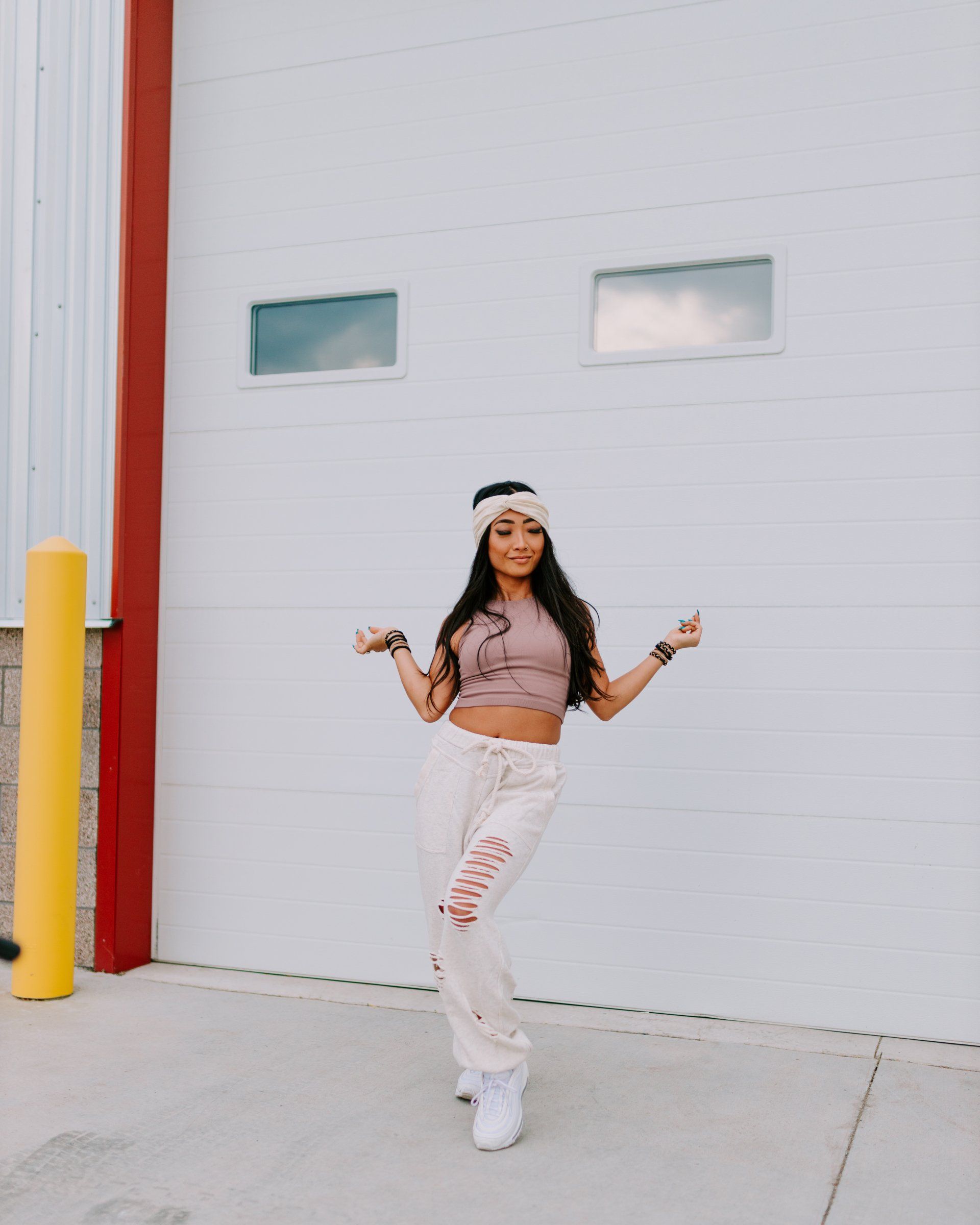 A woman in a crop top and sweatpants is standing in front of a garage door.