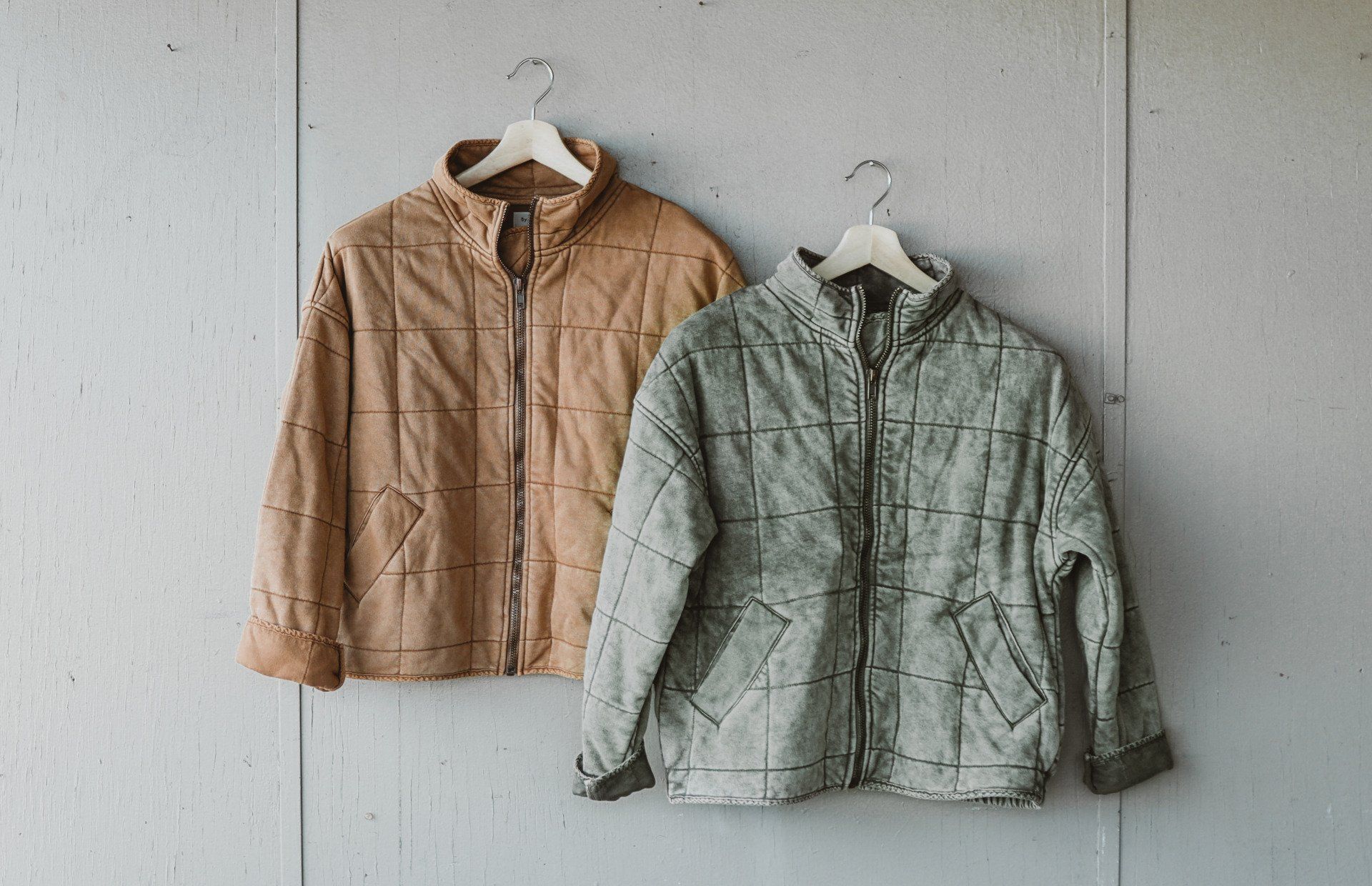 Two jackets are hanging on a hanger on a wall.