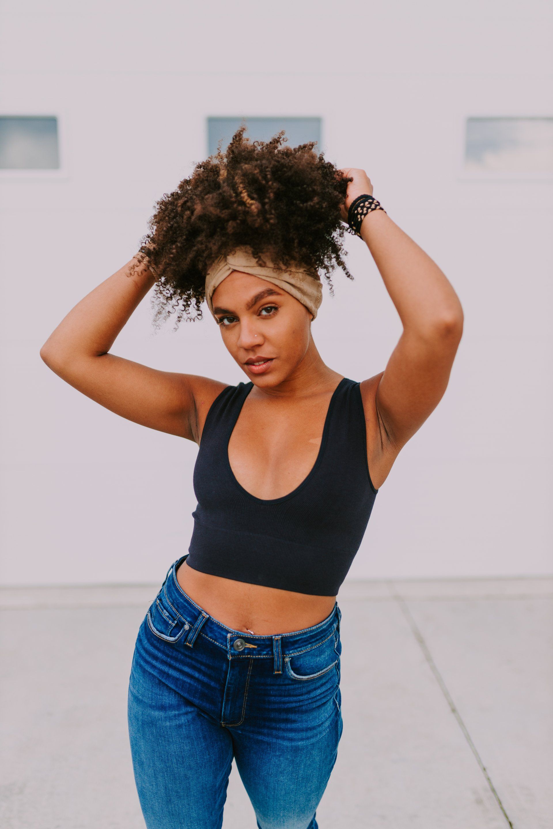 A woman in a black crop top and blue jeans is standing on a sidewalk.