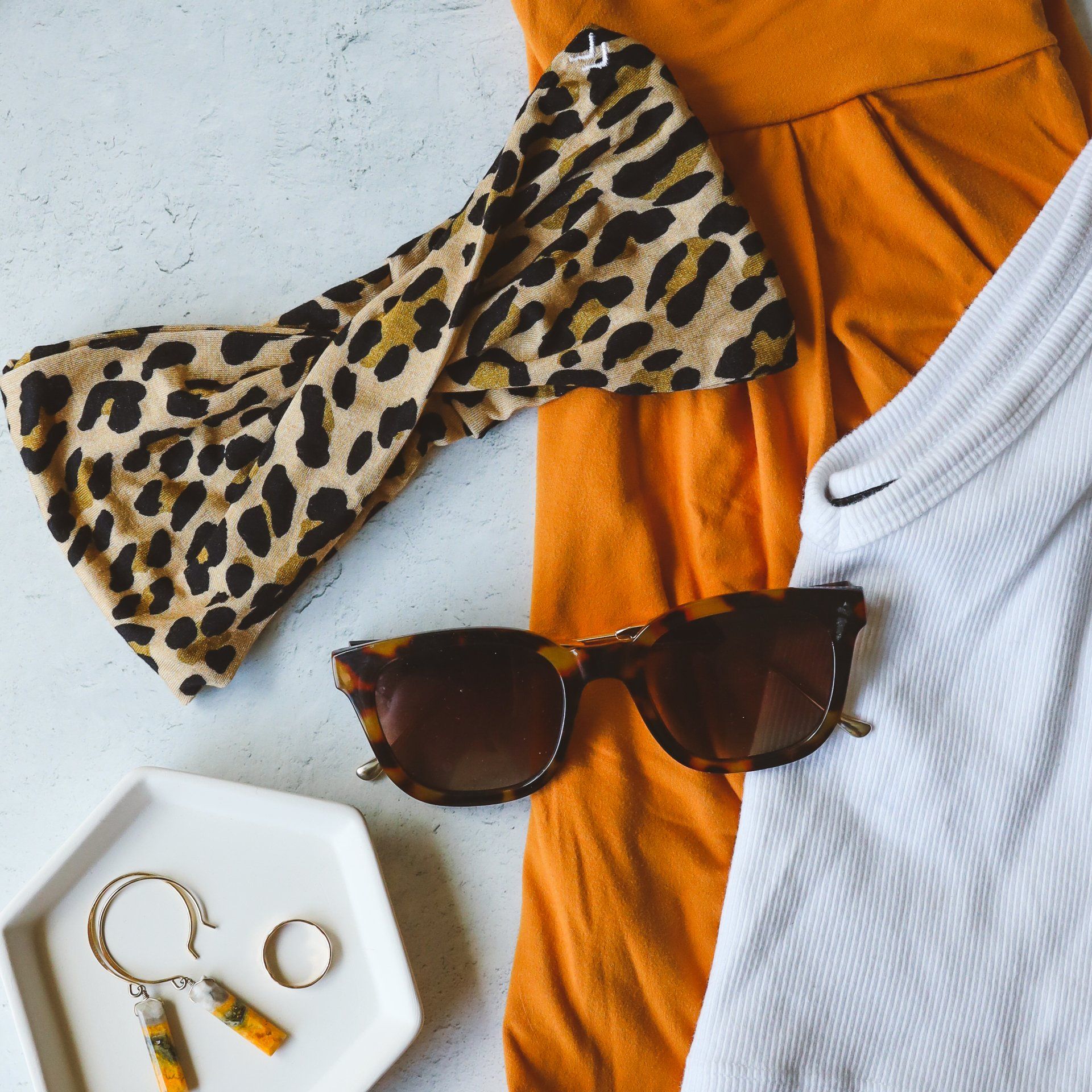A leopard print headband sunglasses earrings and a white shirt on a table