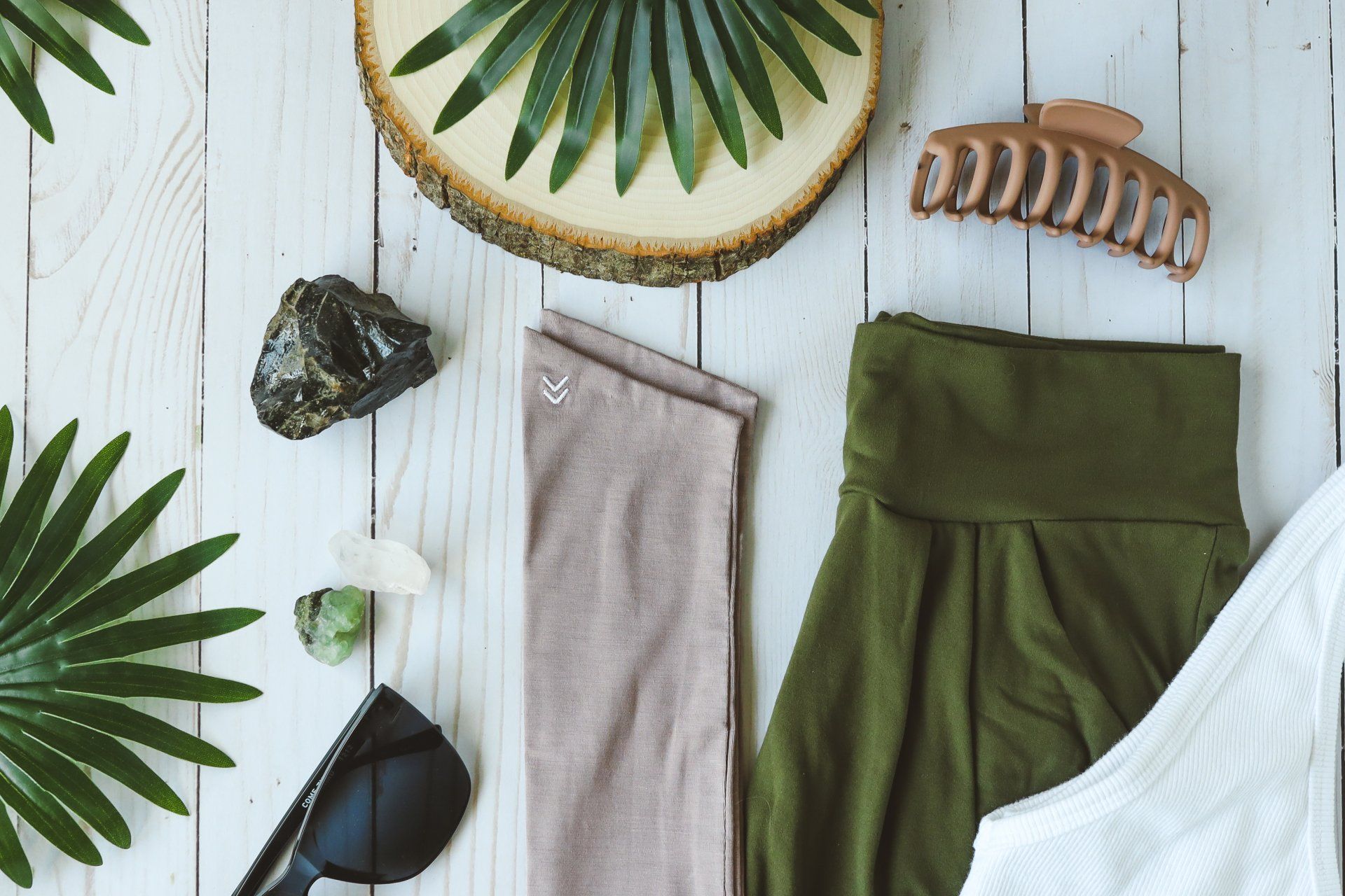 A wooden table topped with clothes , sunglasses , a hair clip , and leaves.