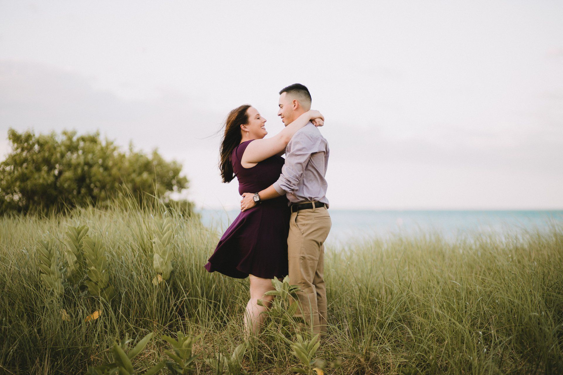 A man and a woman are standing in a field hugging each other.