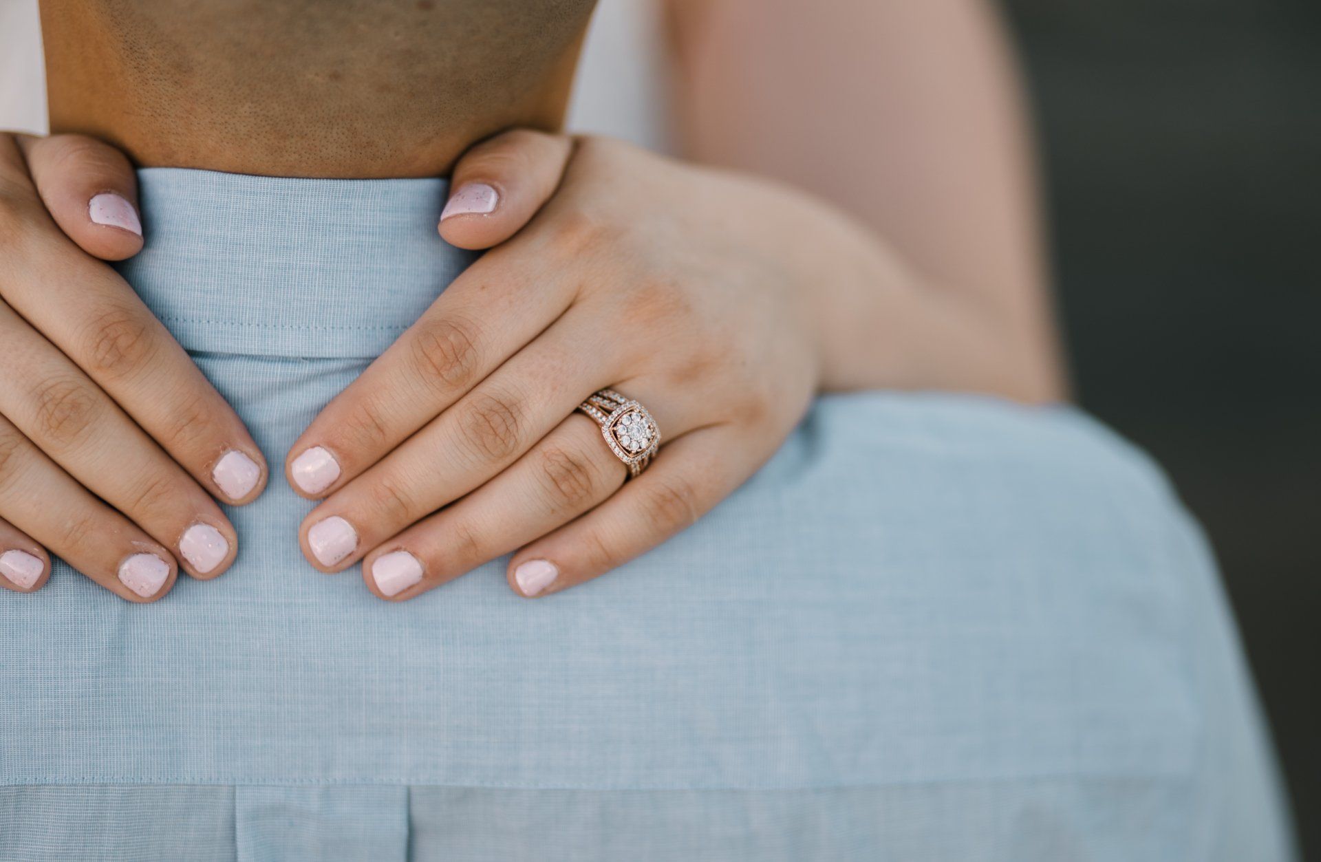 A woman wearing an engagement ring is hugging a man 's neck.