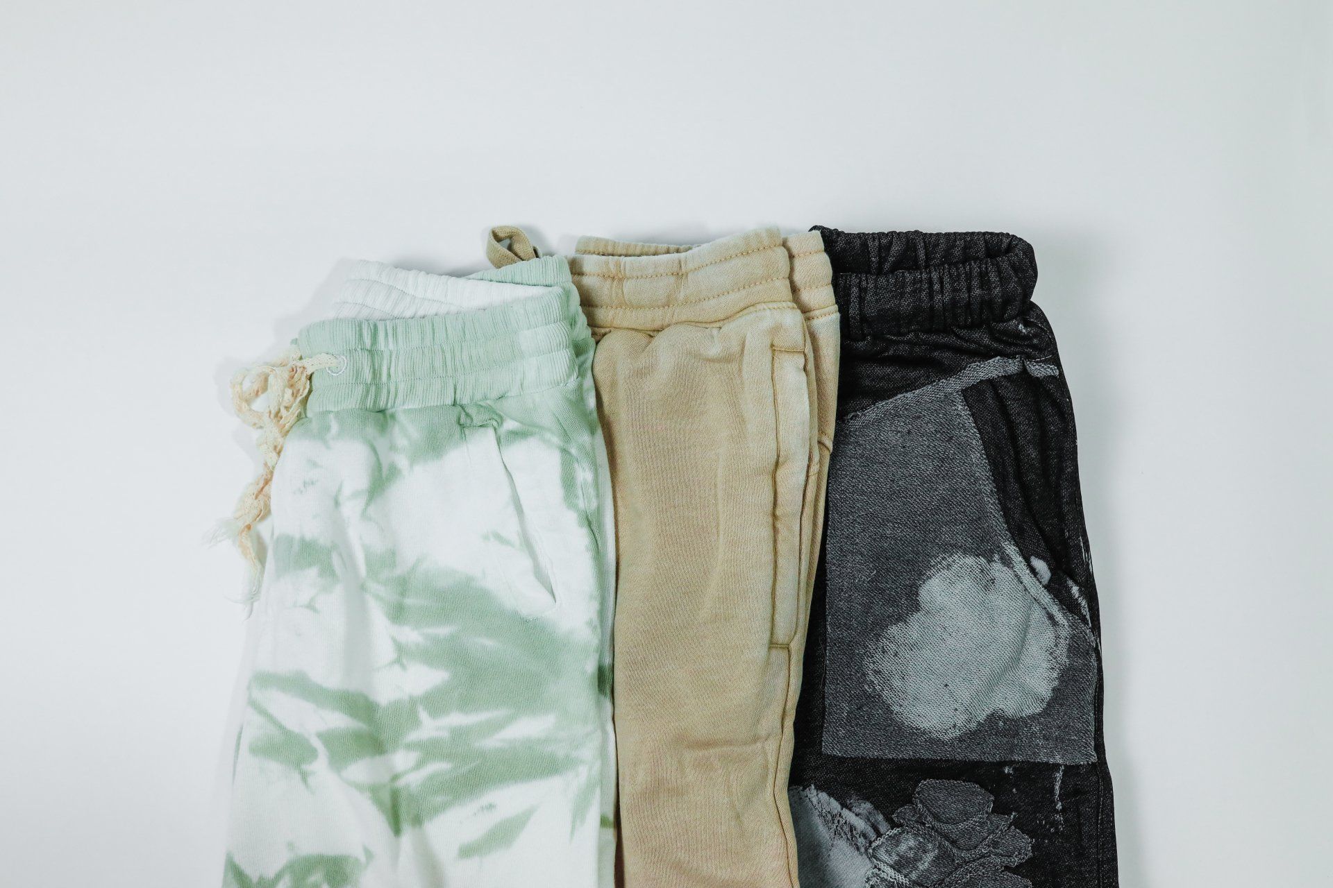 Three pairs of sweatpants are stacked on top of each other on a white surface.