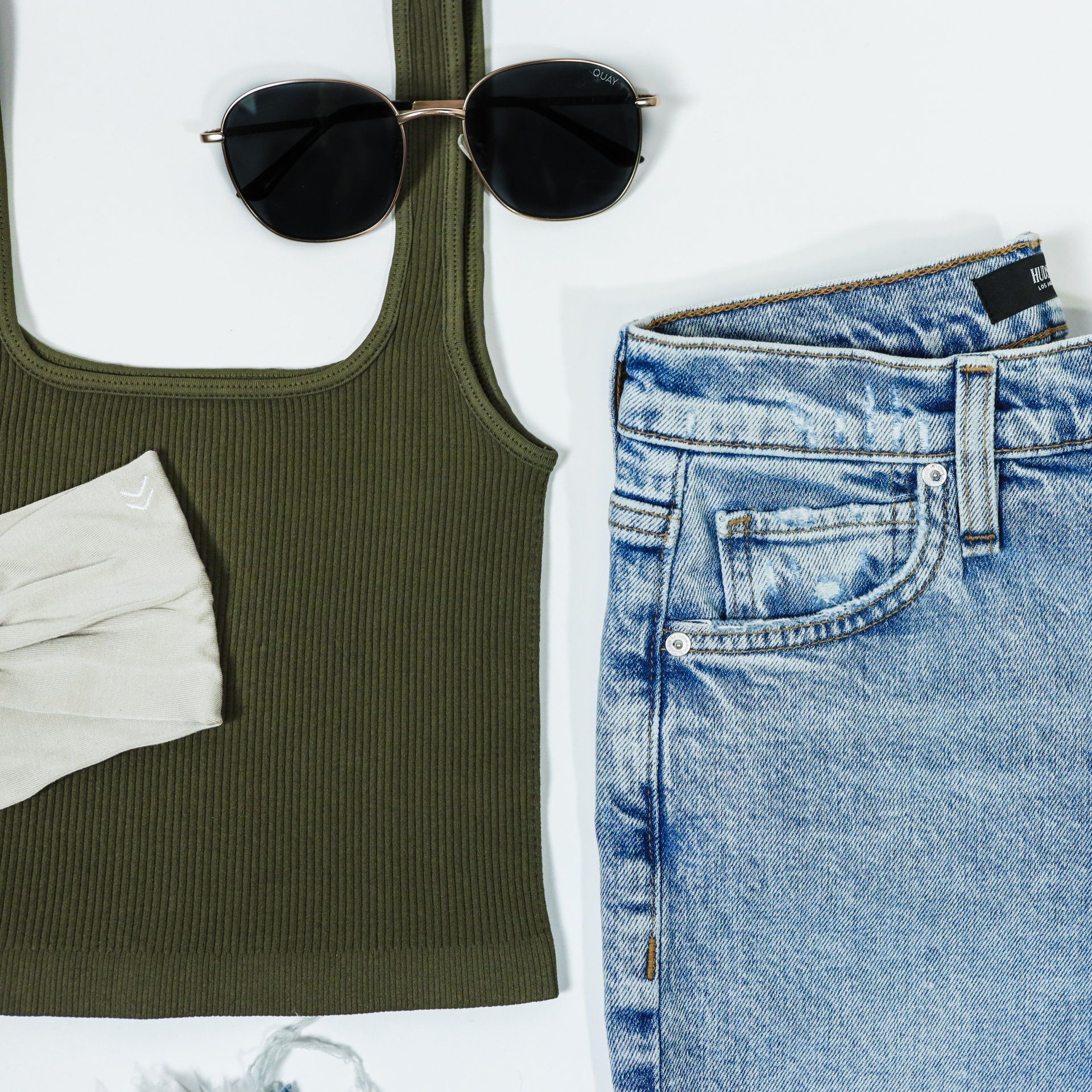 A green tank top , a pair of sunglasses , and a pair of jeans are on a white surface.