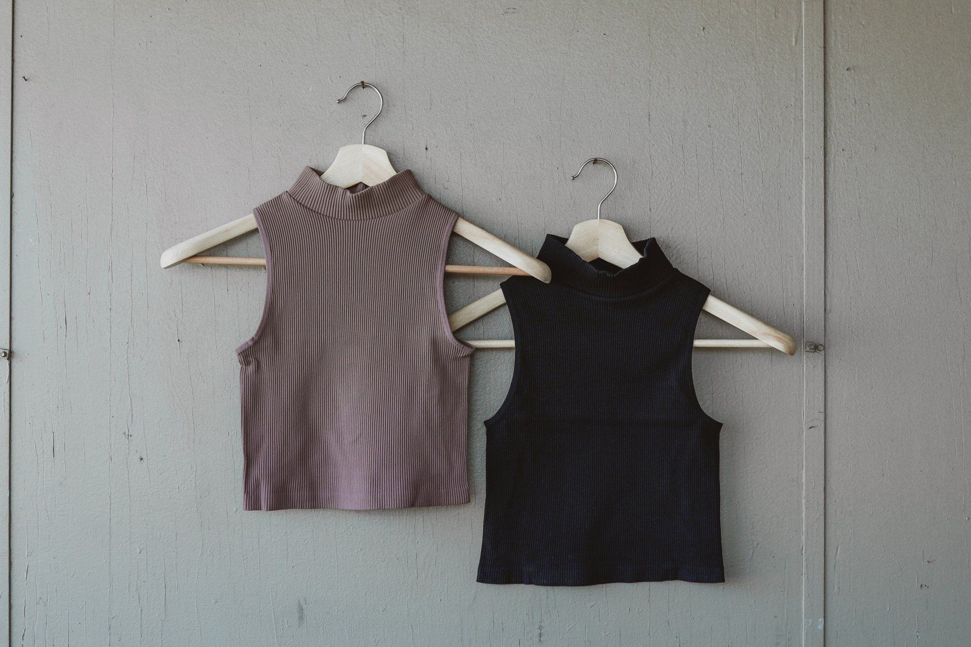 Two tank tops are hanging on wooden hangers on a wall.