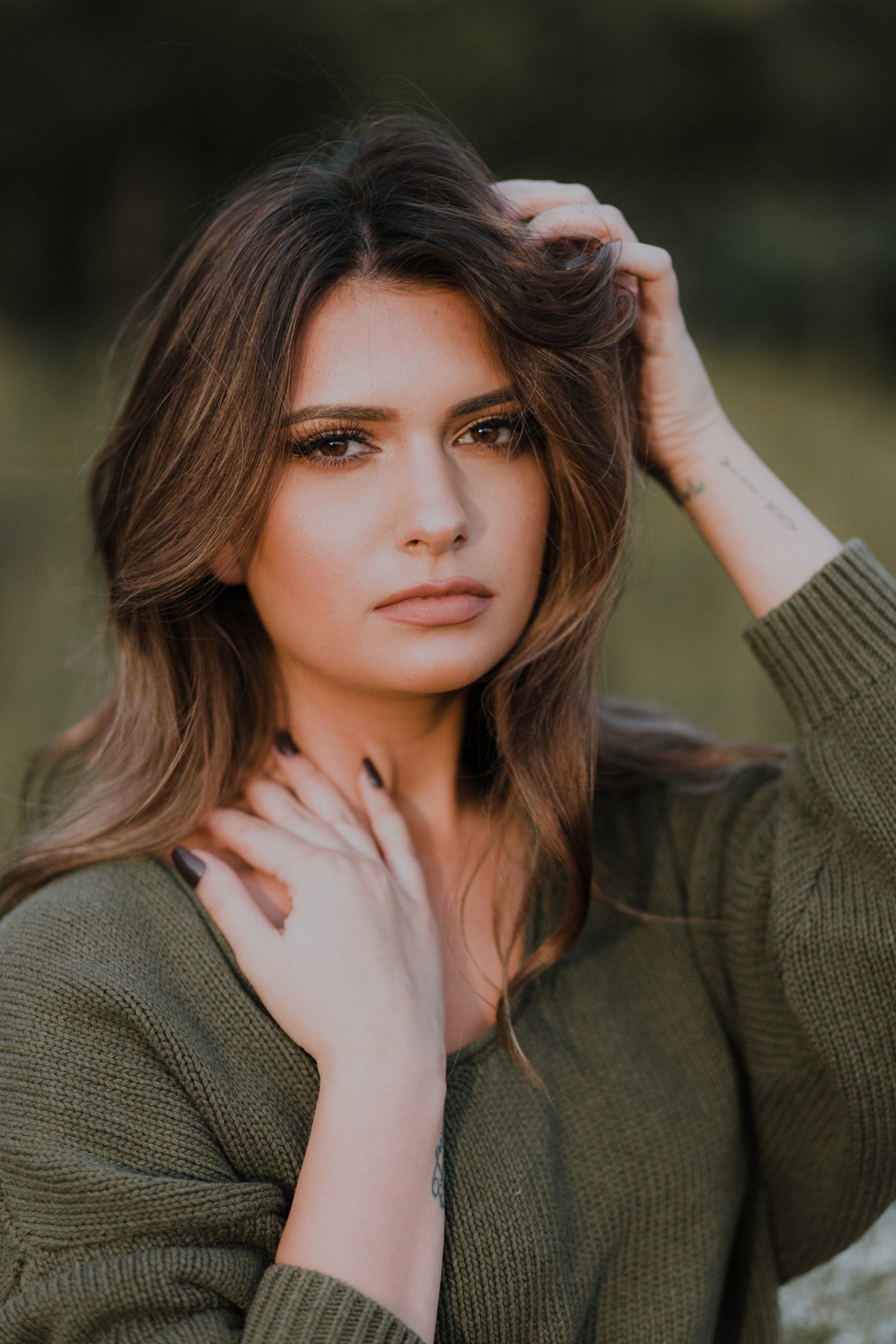 A woman in a green sweater is touching her hair.
