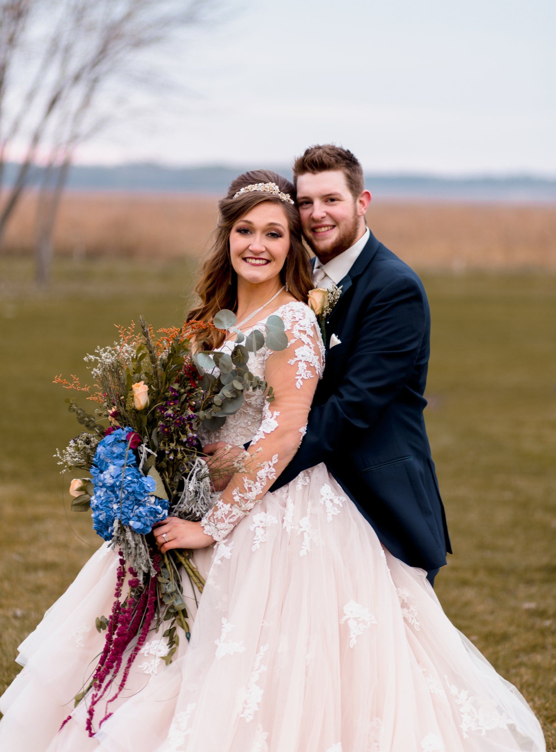 A bride and groom are posing for a picture in a field.