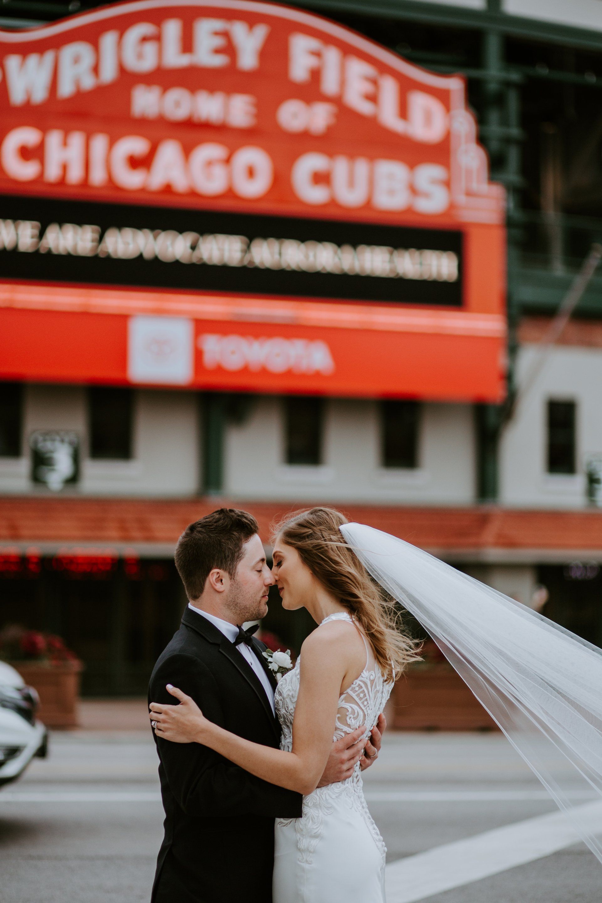 A bride and groom are kissing in front of a chicago cubs sign.