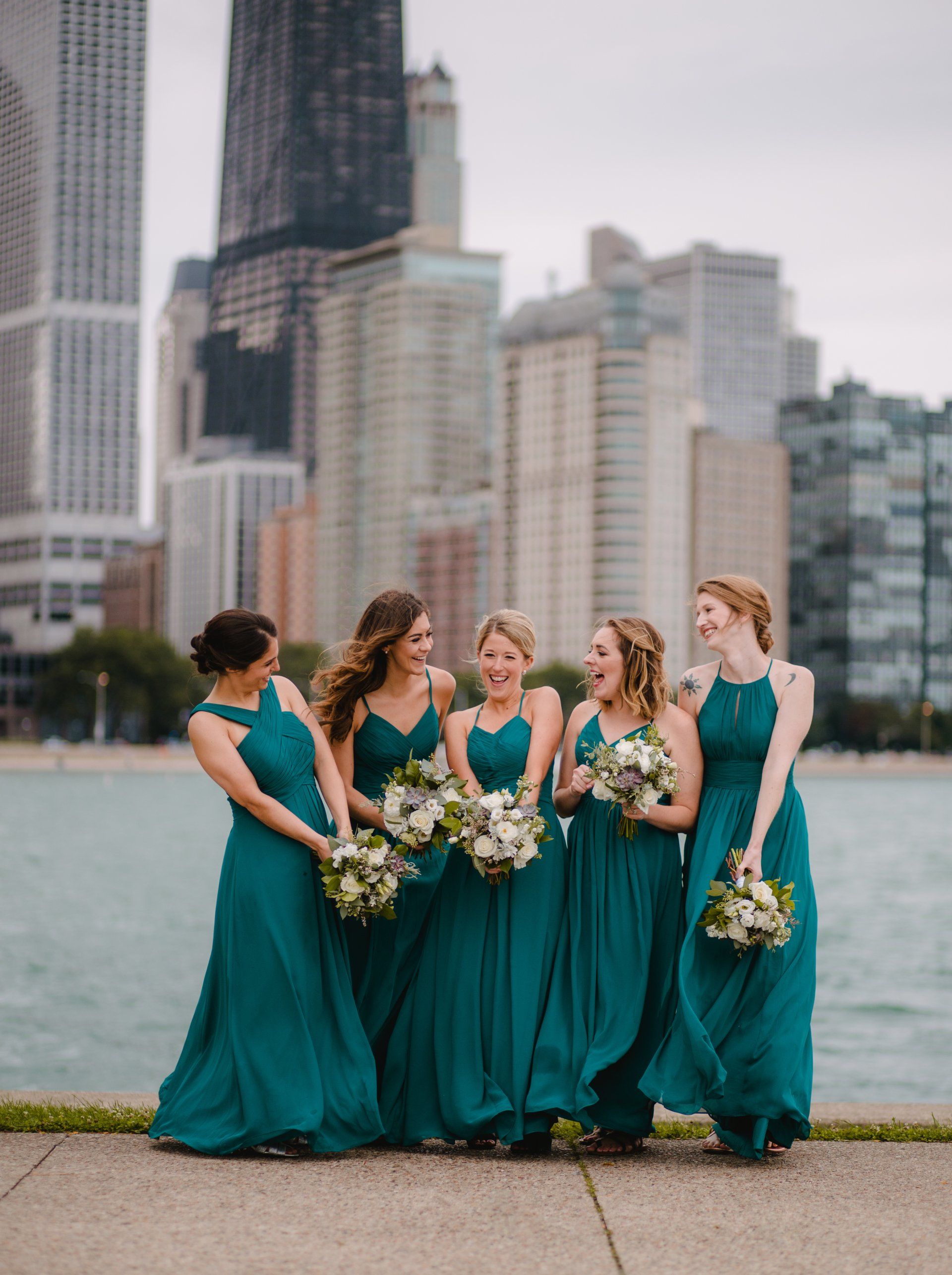 A group of bridesmaids in teal dresses are posing for a picture in front of a city skyline.