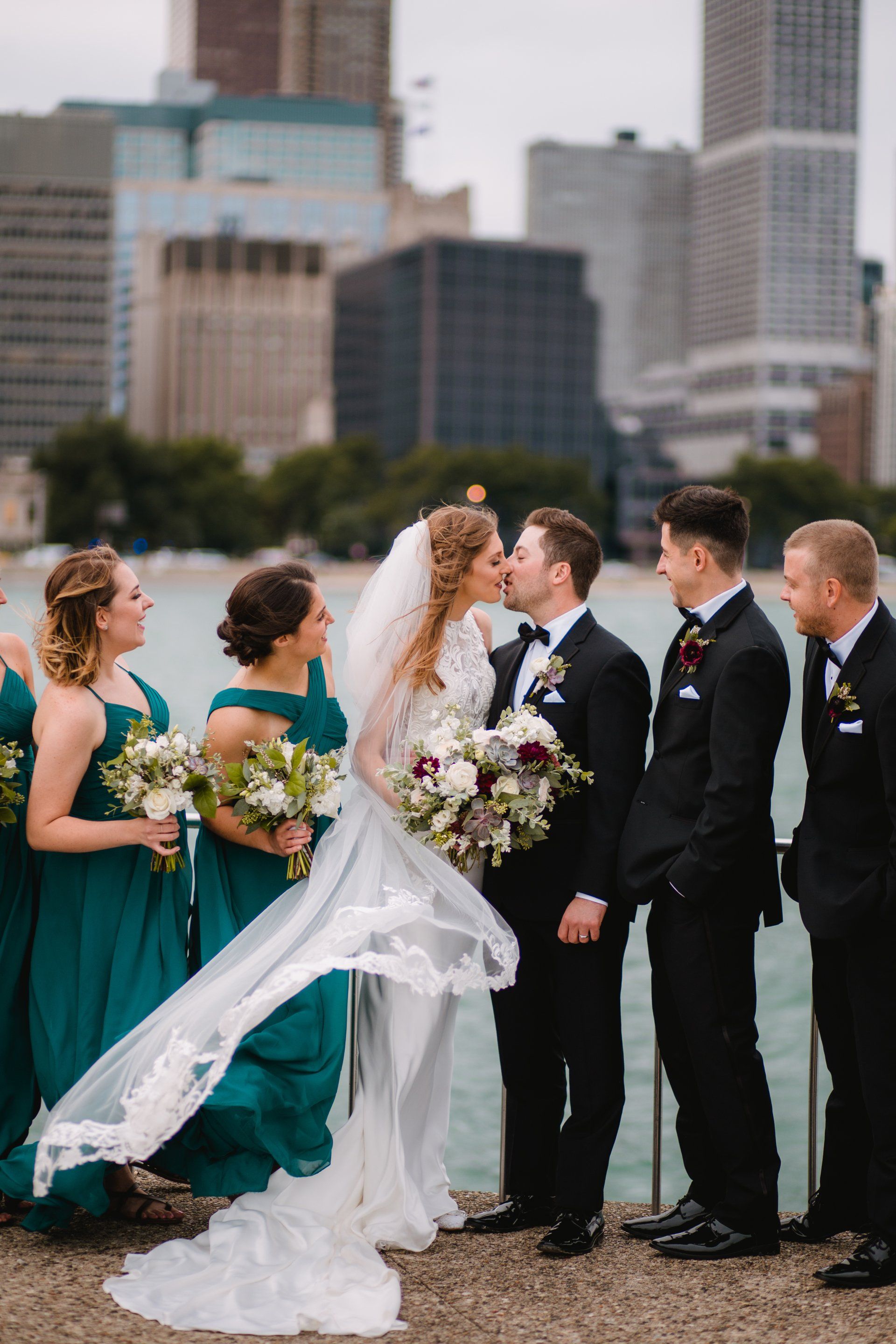 A bride and groom are kissing in front of their wedding party.