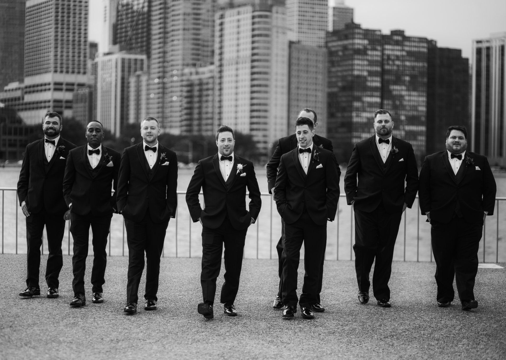 A group of men in tuxedos and bow ties are standing next to each other in front of a city skyline.