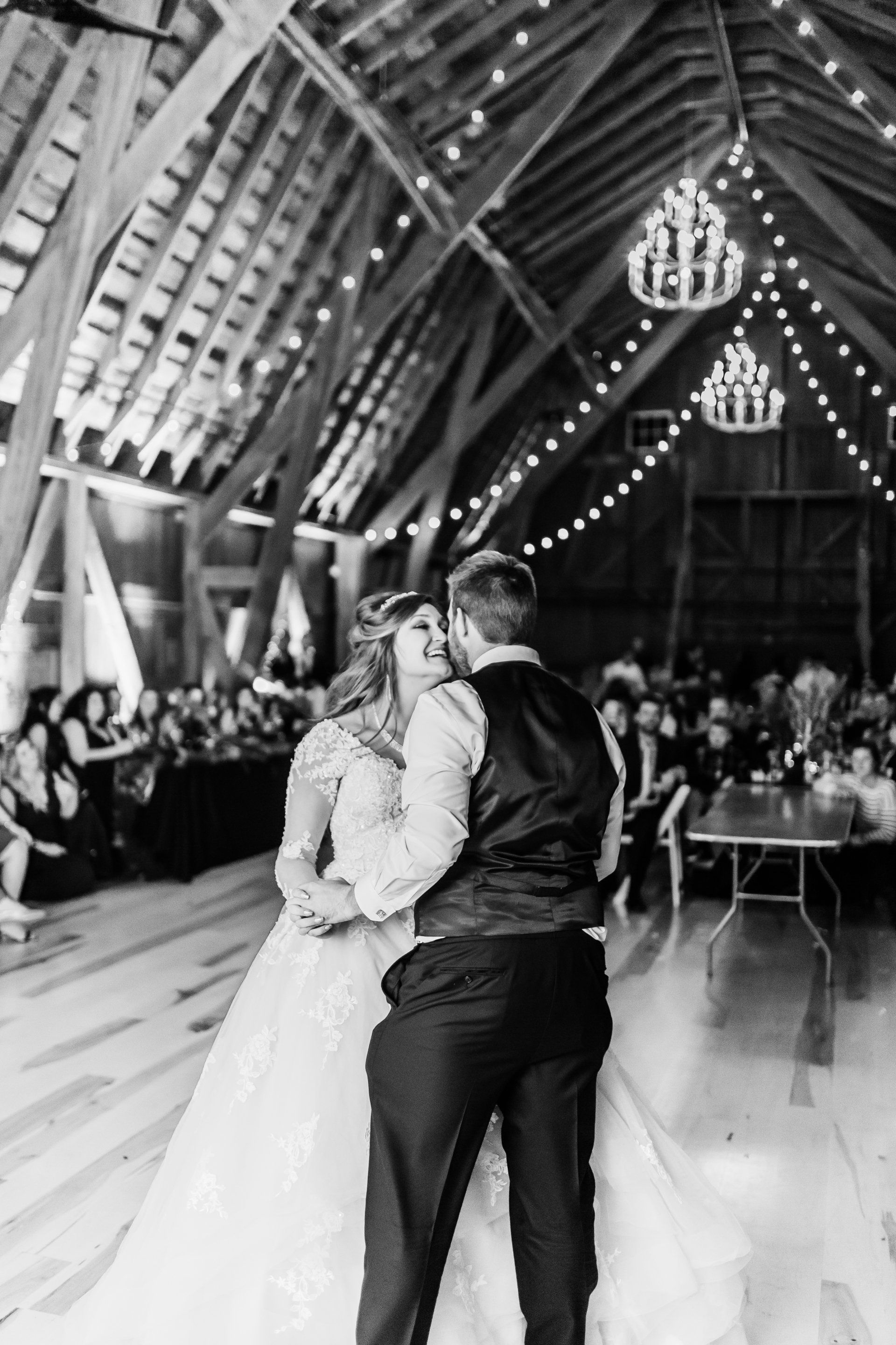 A bride and groom are dancing in a barn at their wedding reception.