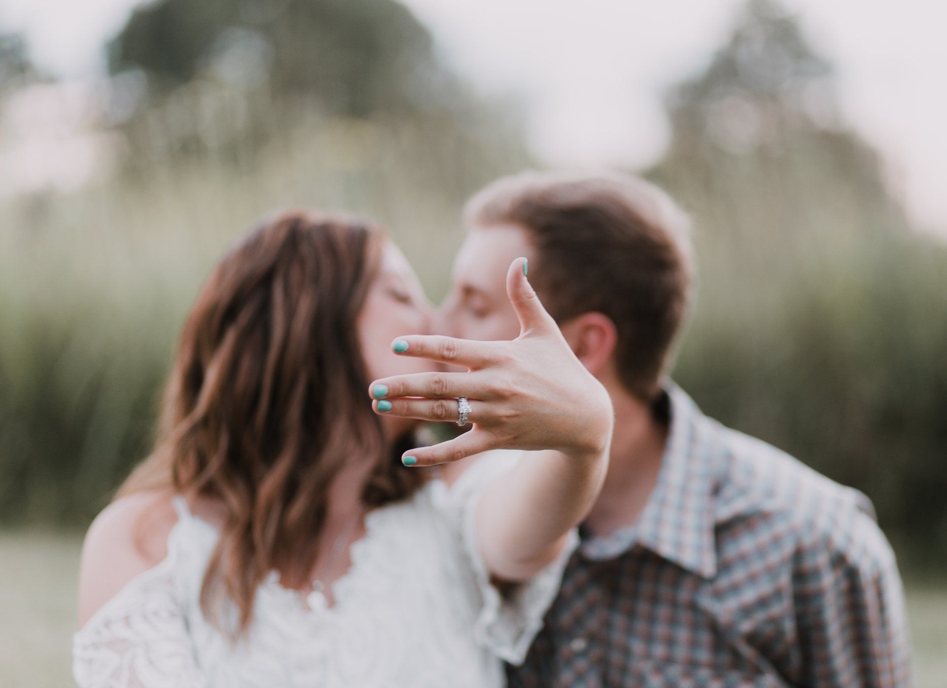 A man and woman are kissing while the woman shows off her engagement ring.